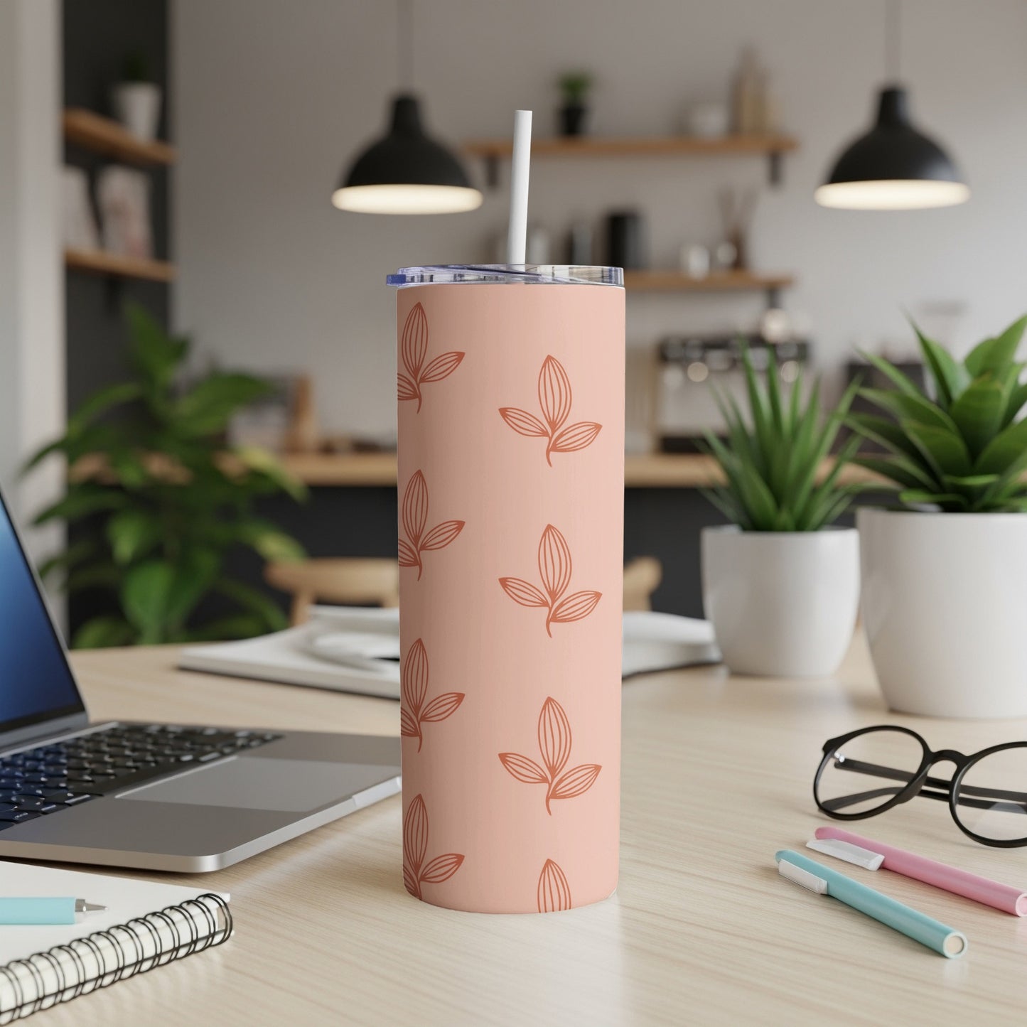 Pale pink tumbler with leaf pattern and white straw on desk.