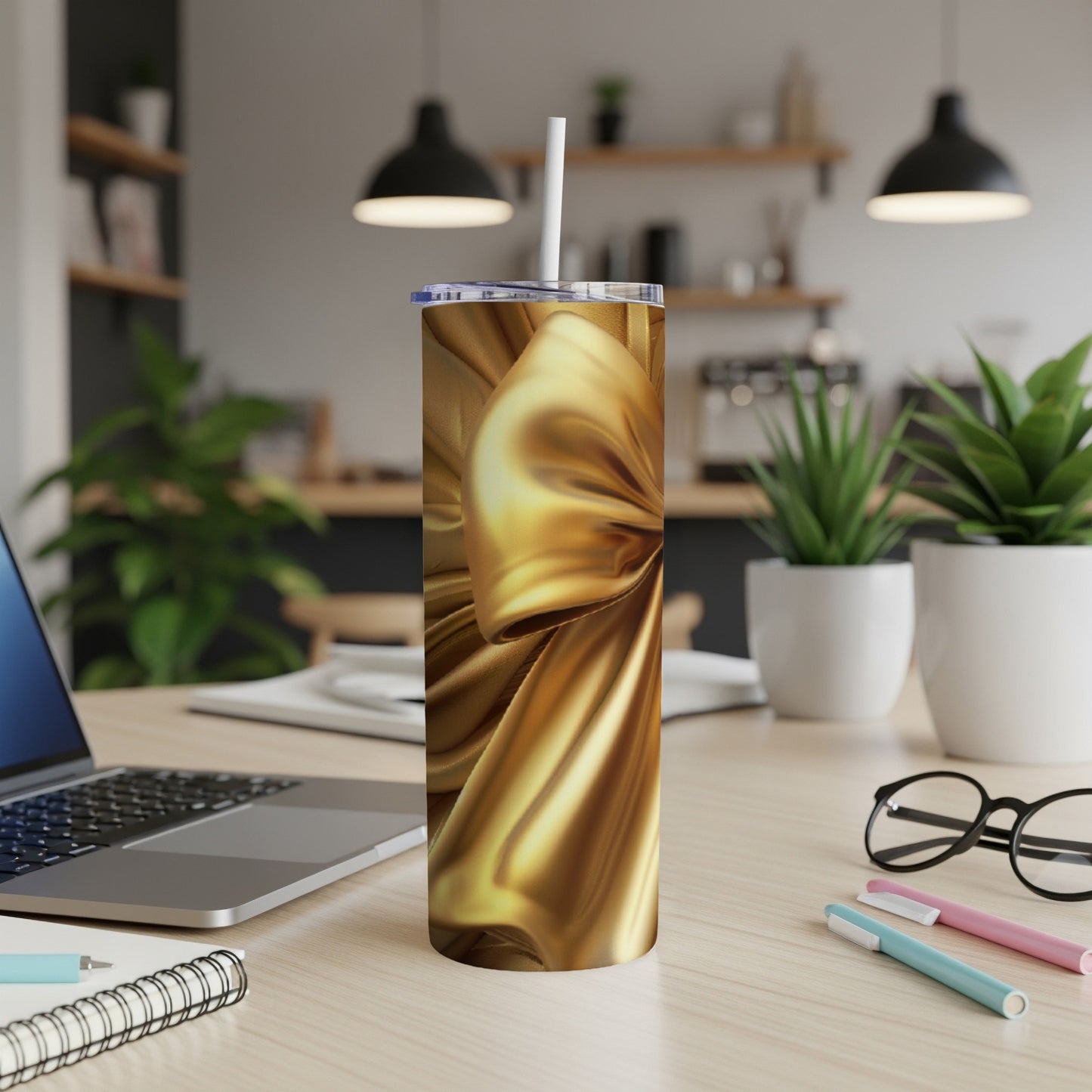 Gold satin ribbon on a skinny tumbler with a straw, on a desk.