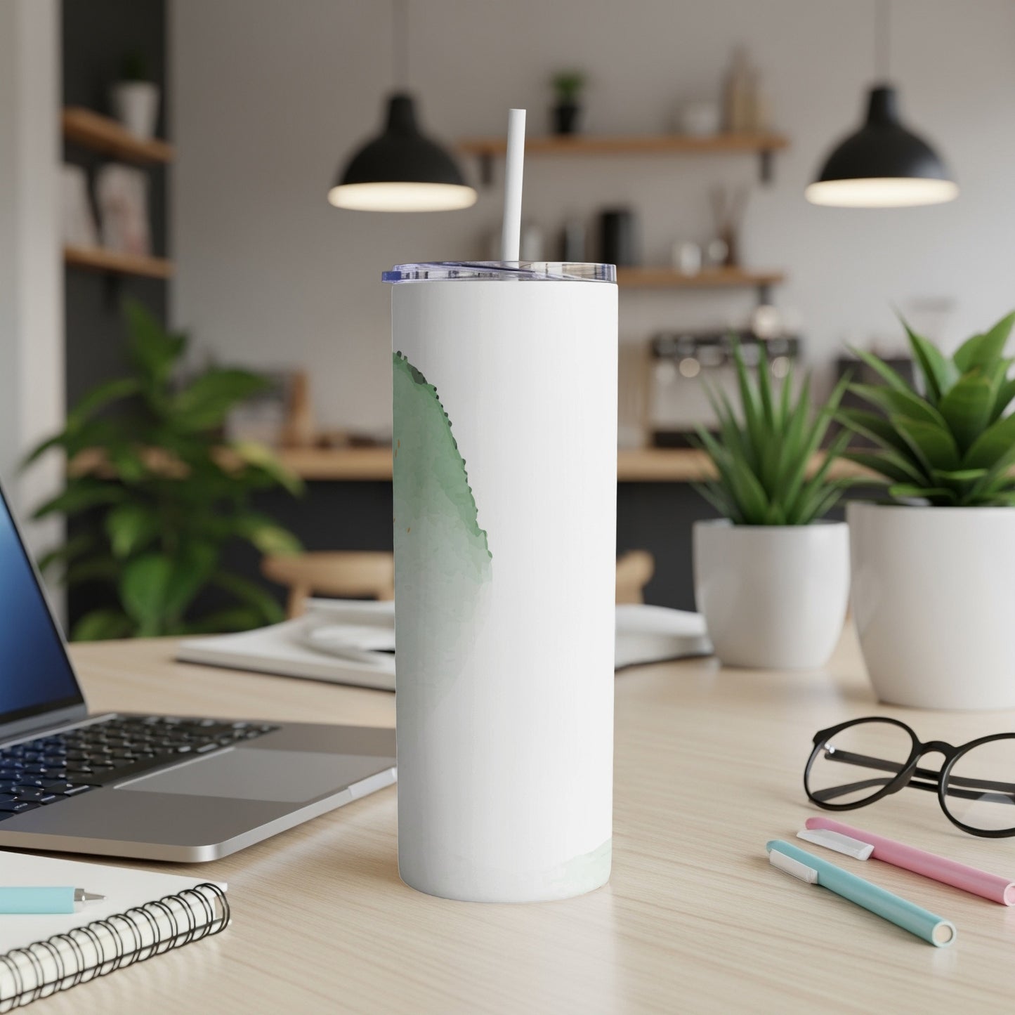 White tumbler with green abstract design and straw, on a desk.