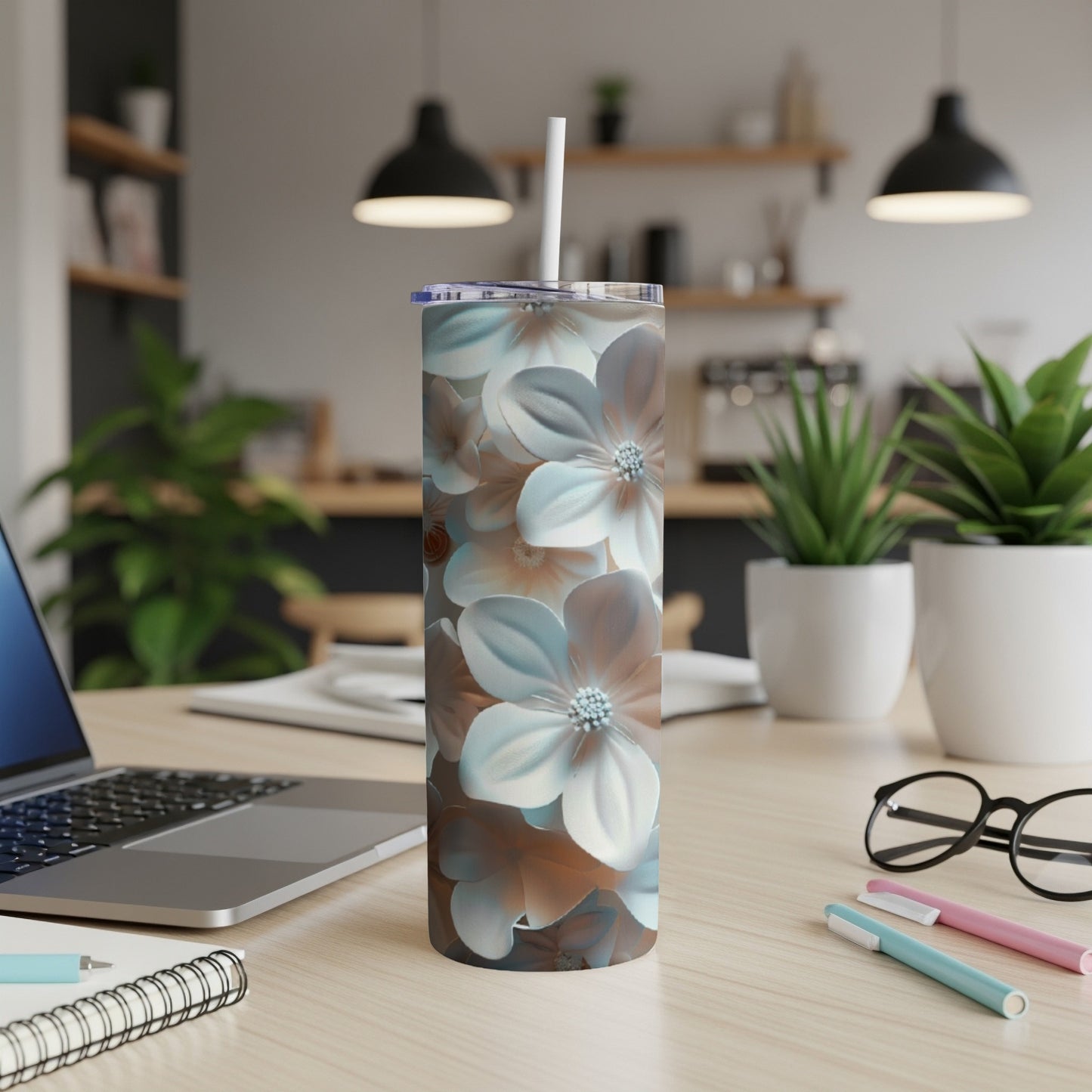 Tall floral tumbler with straw on a wooden desk next to a laptop.