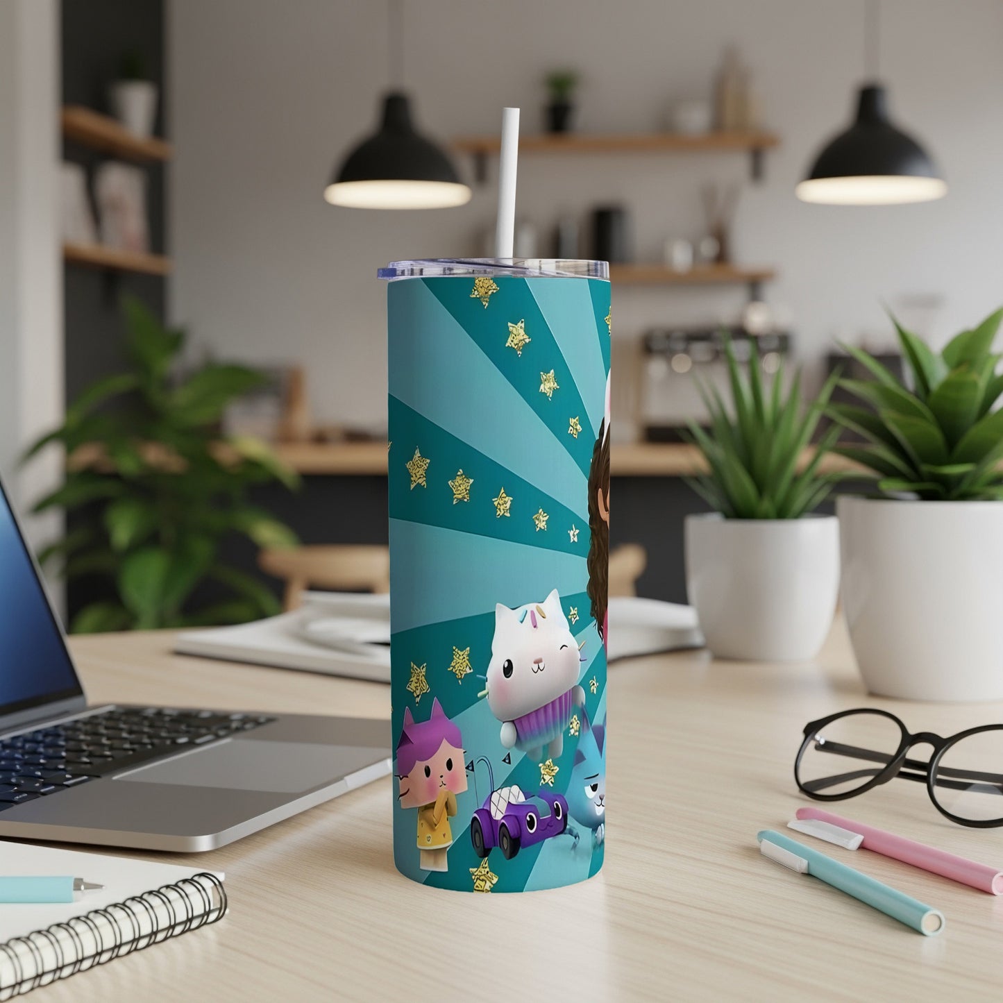 Teal tumbler with cartoon cat characters and gold stars, on a desk.