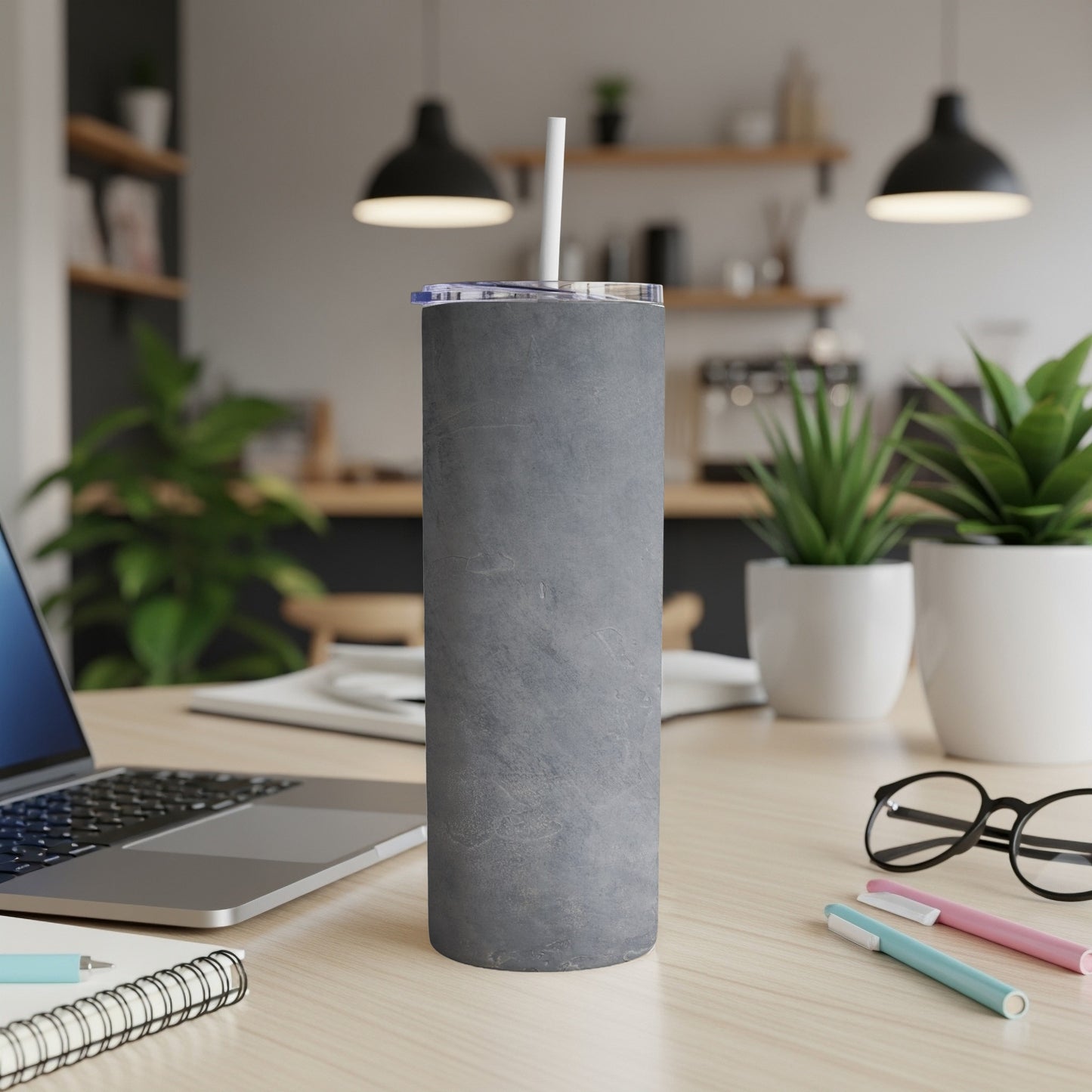 Gray textured tumbler with straw on a desk next to a laptop.