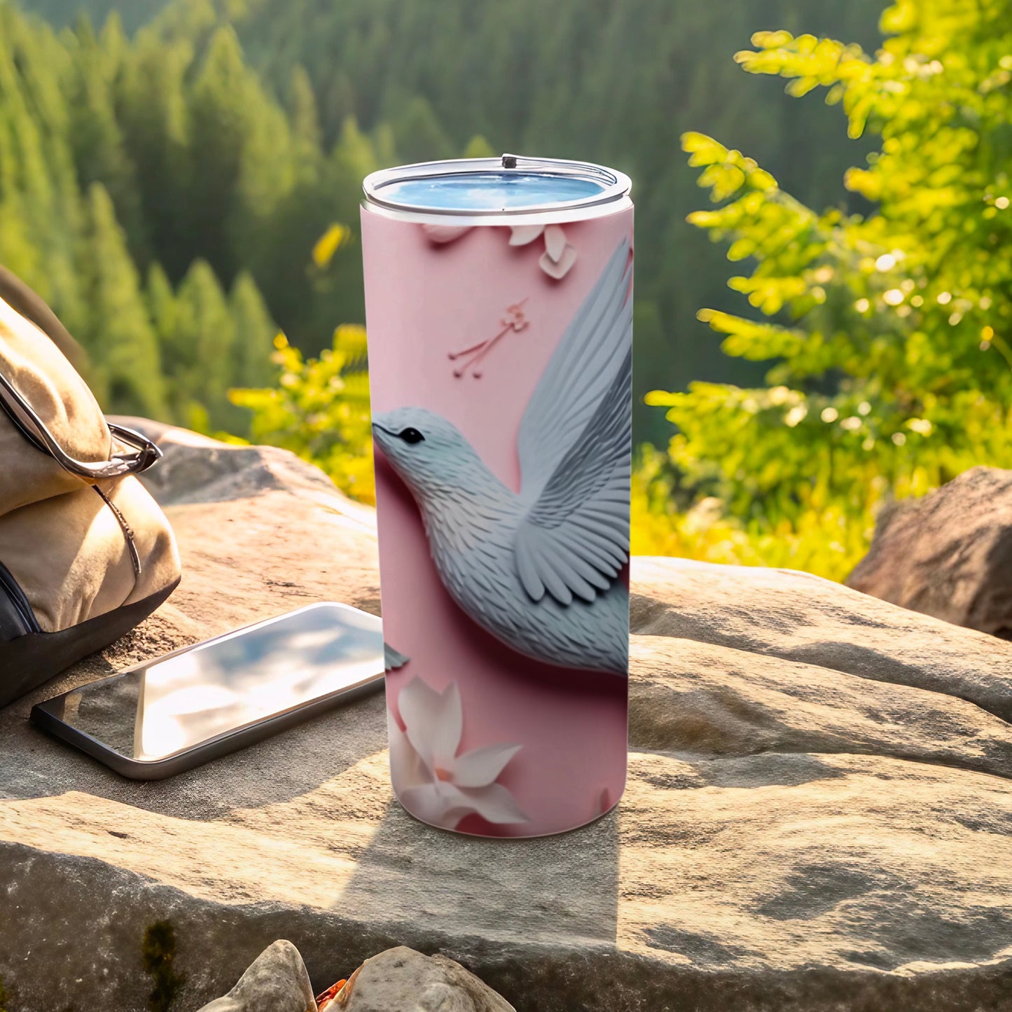 Pink tumbler with white bird and flower design, resting on rocks.