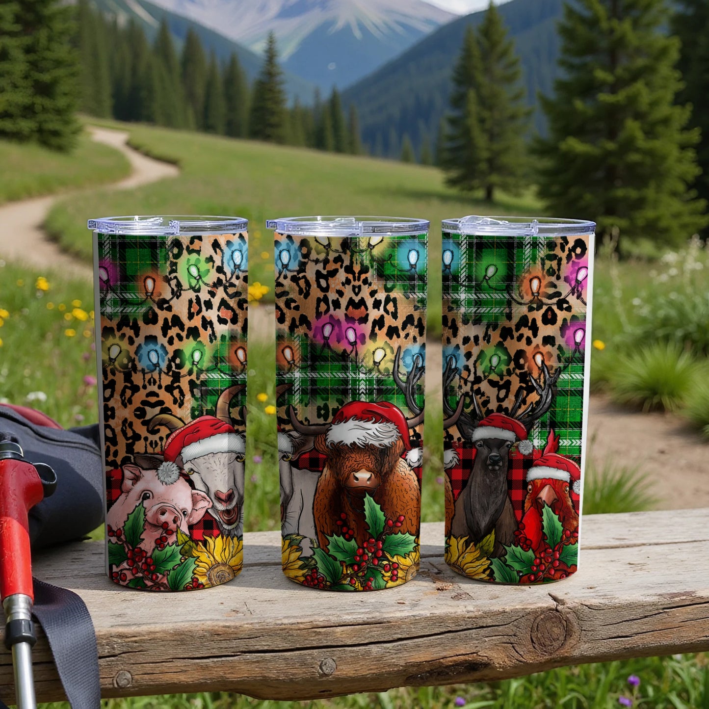 Three tumblers with festive animal designs and holiday lights sit on a wooden surface.