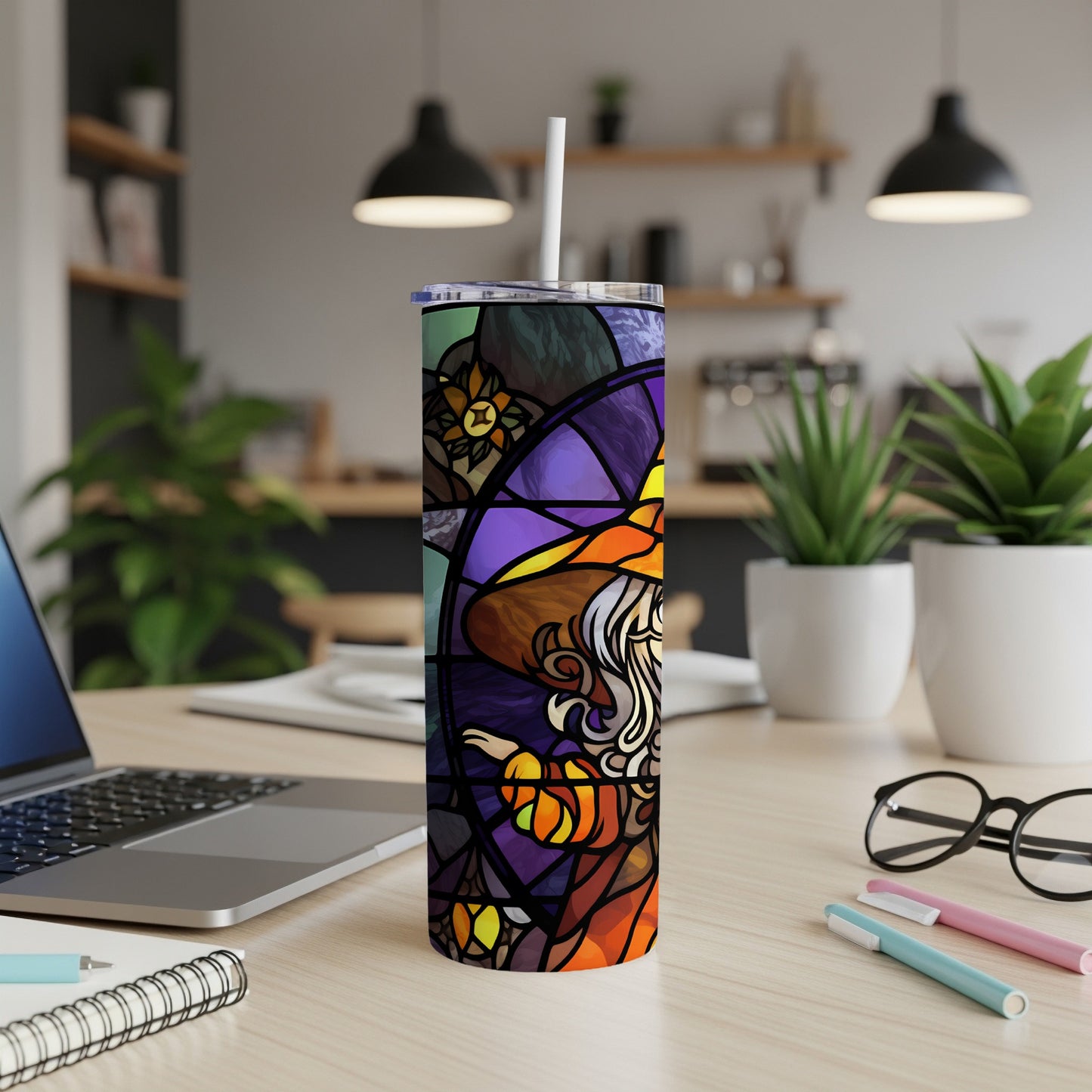 Stained glass witch and pumpkin tumbler with straw on desk.