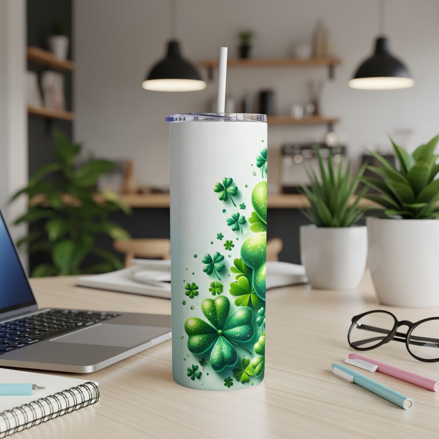 White tumbler with shamrocks and glitter accents, with straw, on a desk.