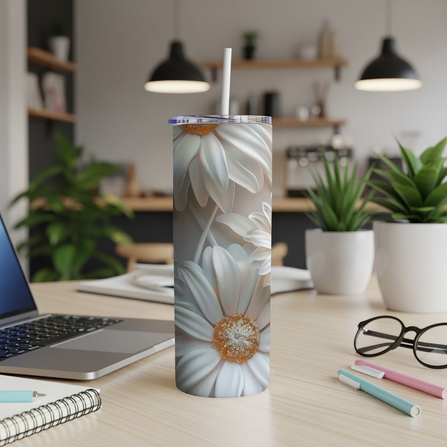 White daisy tumbler with straw on a desk with laptop and pens.