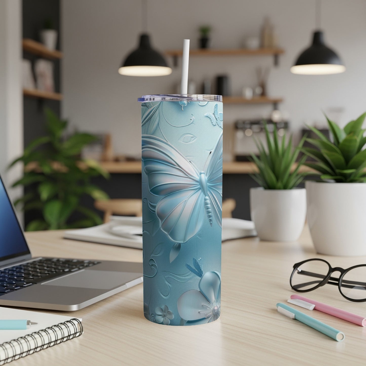 Blue butterfly and floral patterned tumbler with a straw, on a desk.