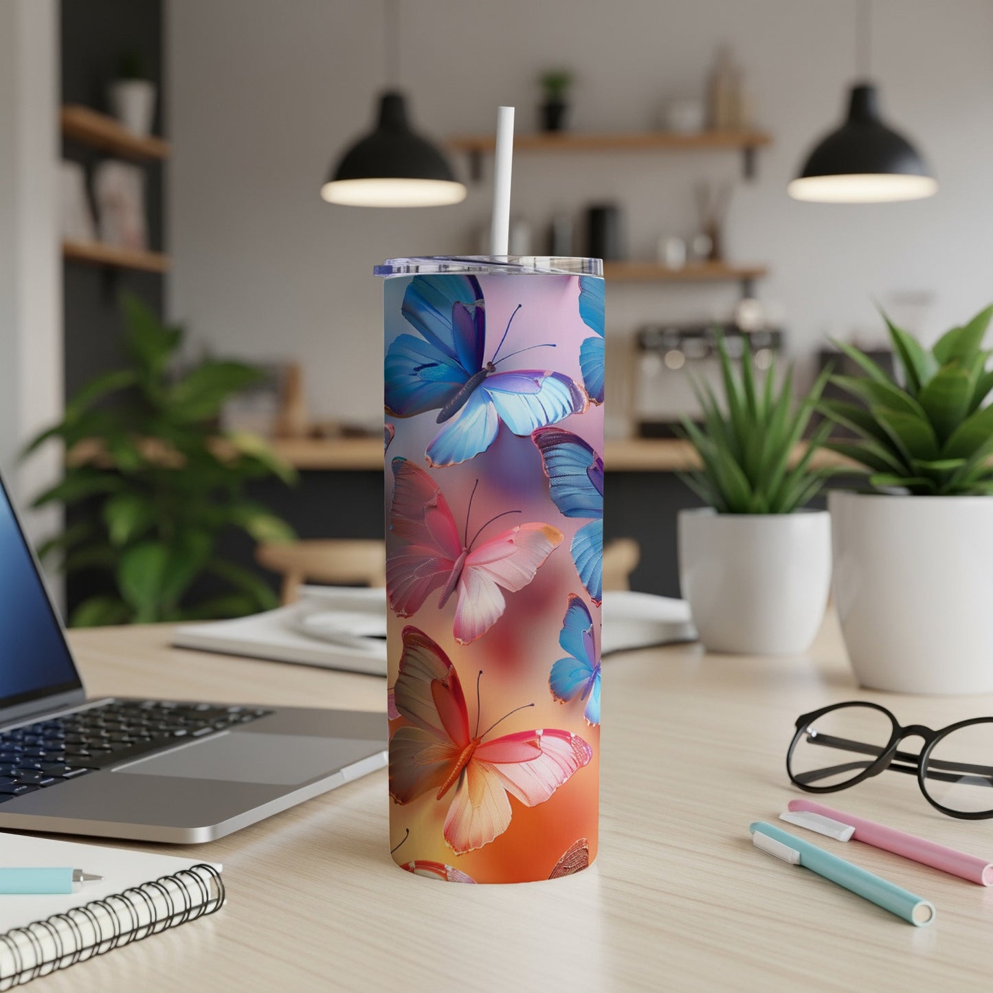 Tall tumbler with colorful butterflies on a desk with a laptop.