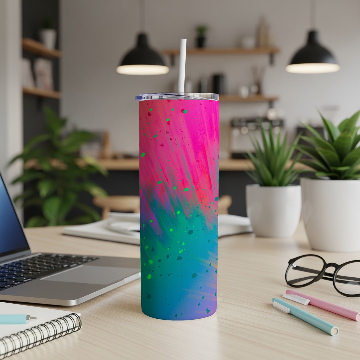 Tumbler with pink, blue, and green abstract splatter design in an office setting.