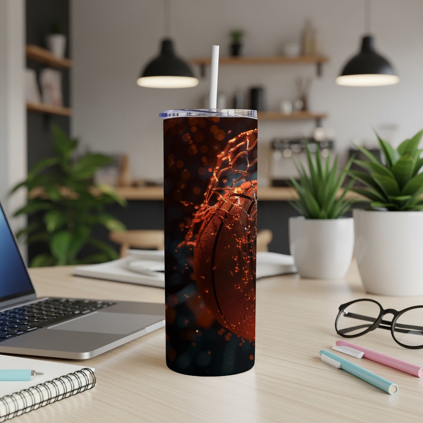 Basketball in net with straw in tumbler, laptop and glasses on desk.