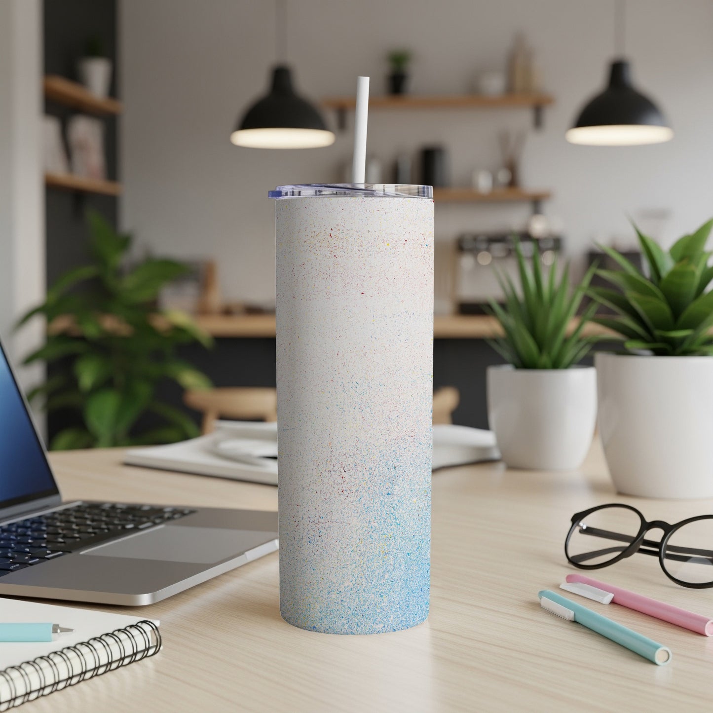 White speckled tumbler with straw on a desk next to a laptop.