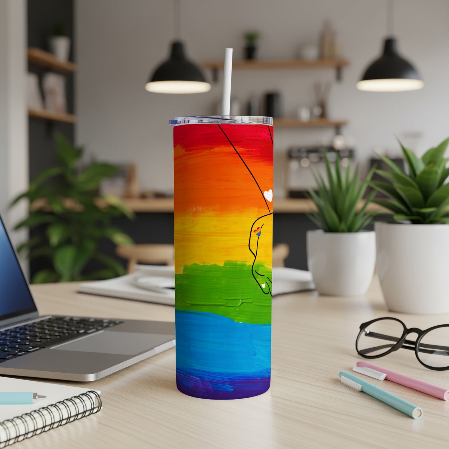 Rainbow tumbler with hand-drawn hearts and a straw on a desk.