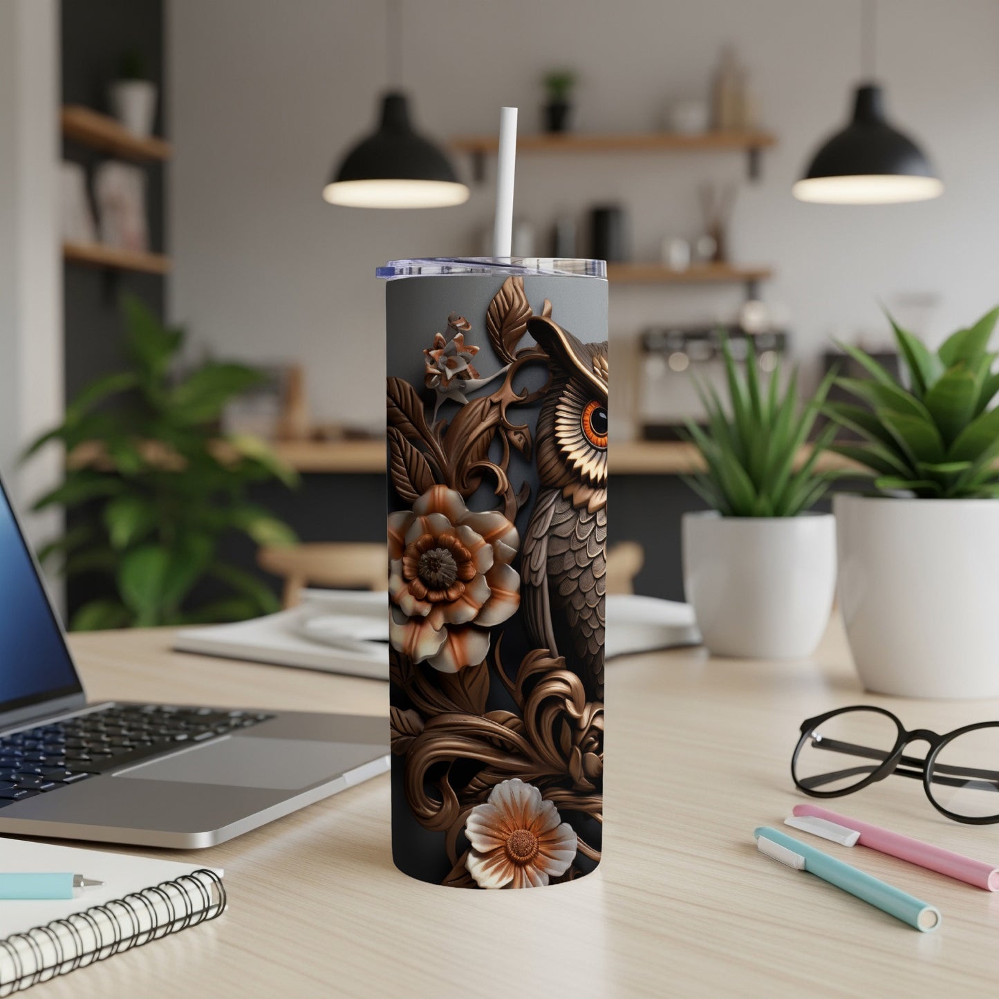 Silver tumbler with owl and floral embossed design on desk.