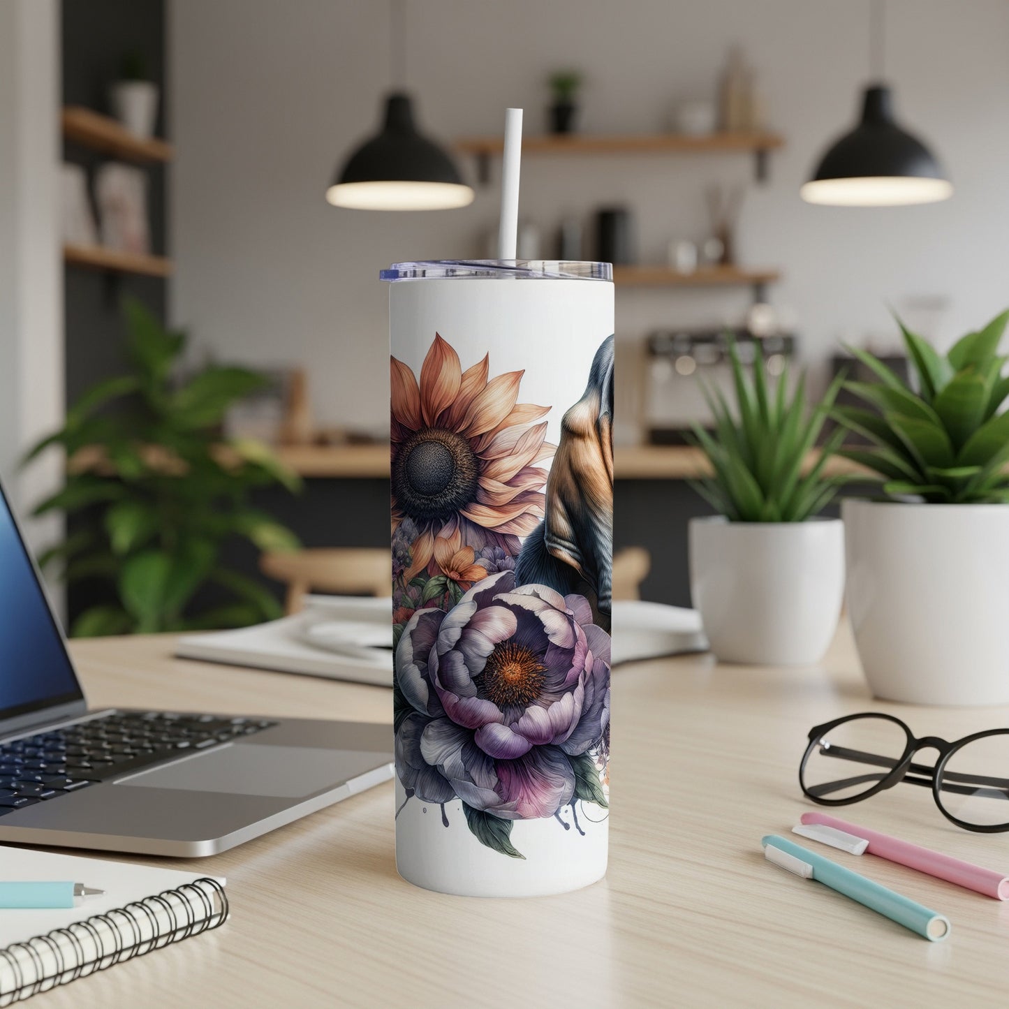 White tumbler with floral and dog illustration, on a desk.