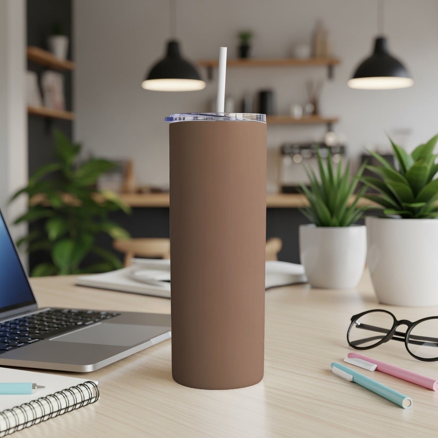 Brown tumbler with straw on desk next to laptop and pens.