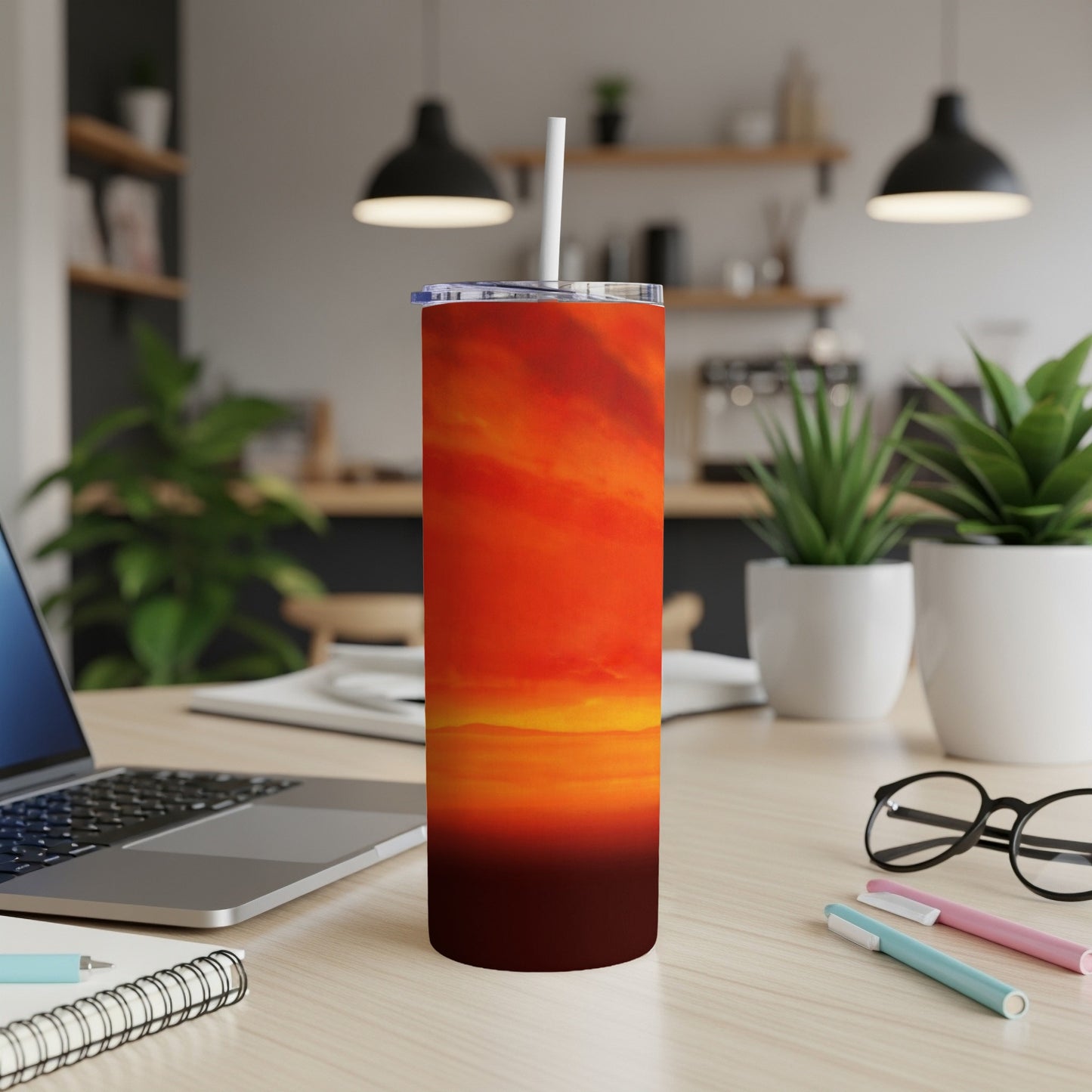 Orange and red abstract sunset design on a stainless steel tumbler with a straw.