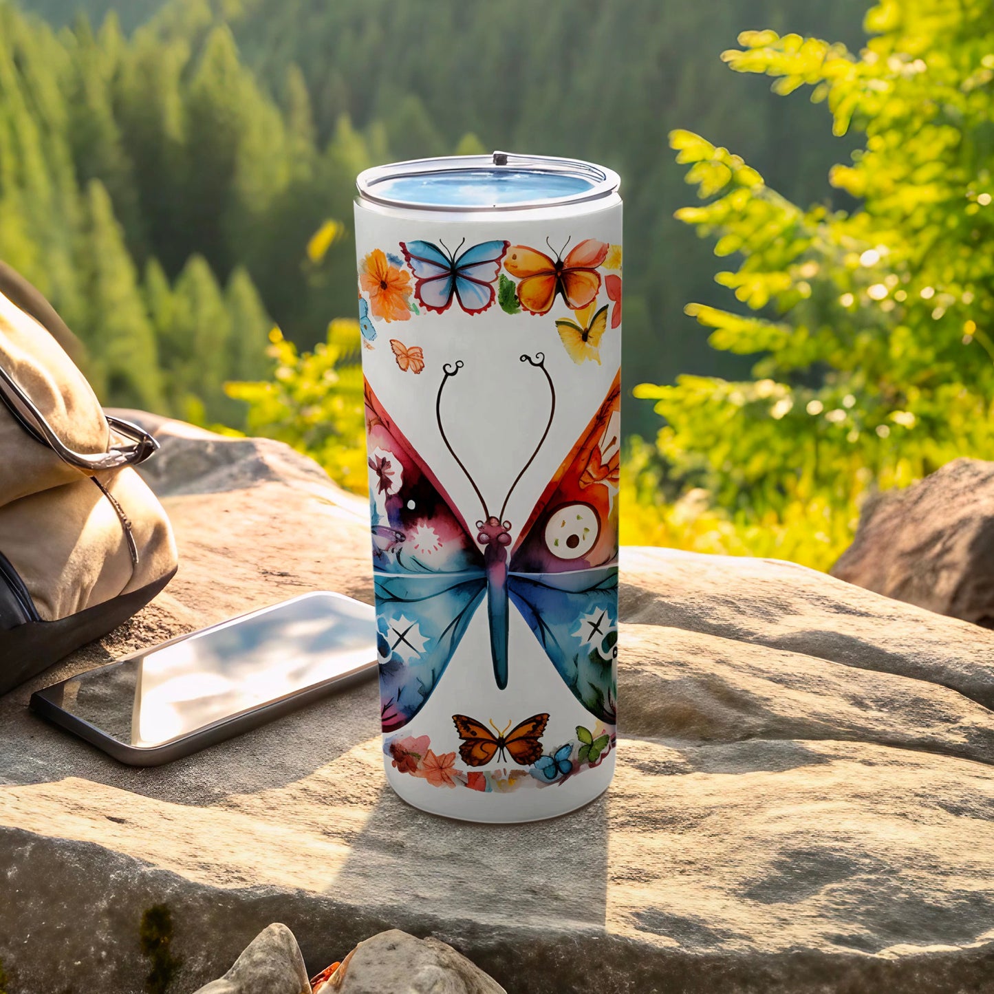 Tumbler with a colorful butterfly design on a rock with a backpack and phone.