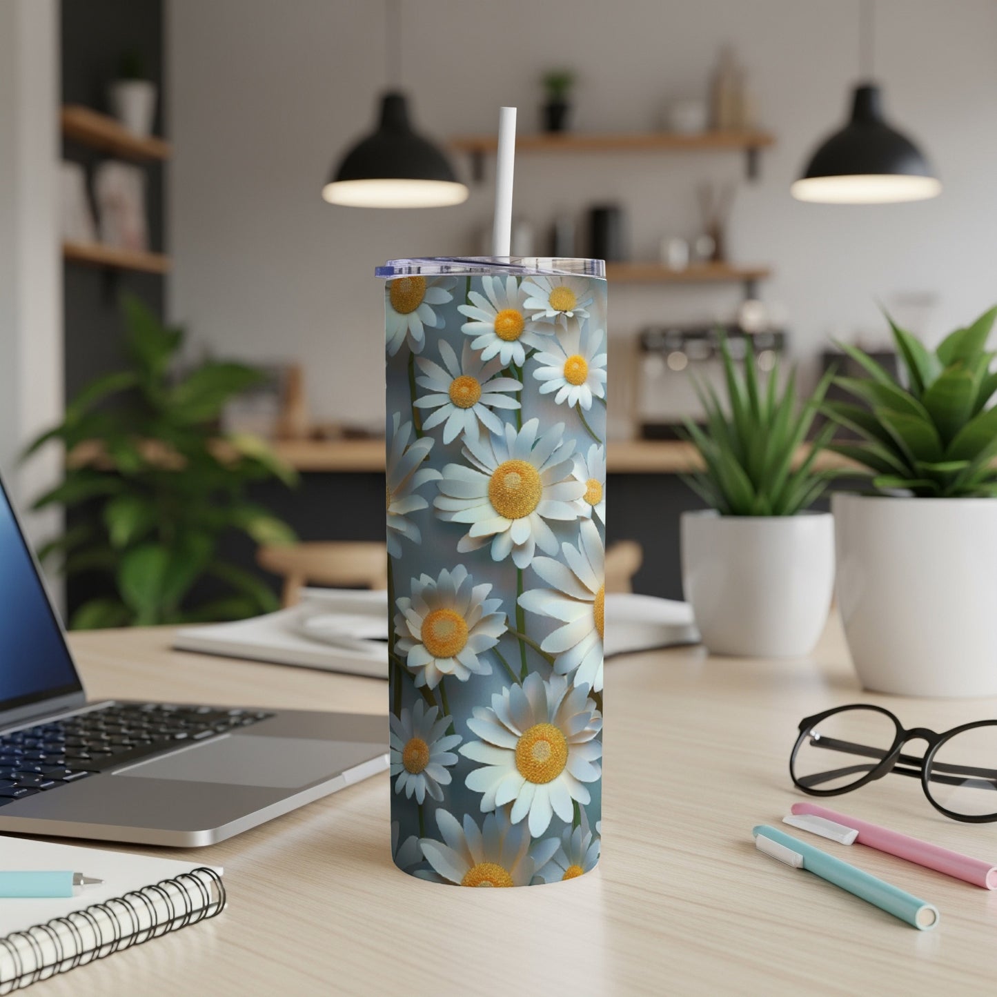 Daisy pattern skinny tumbler with straw on desk.