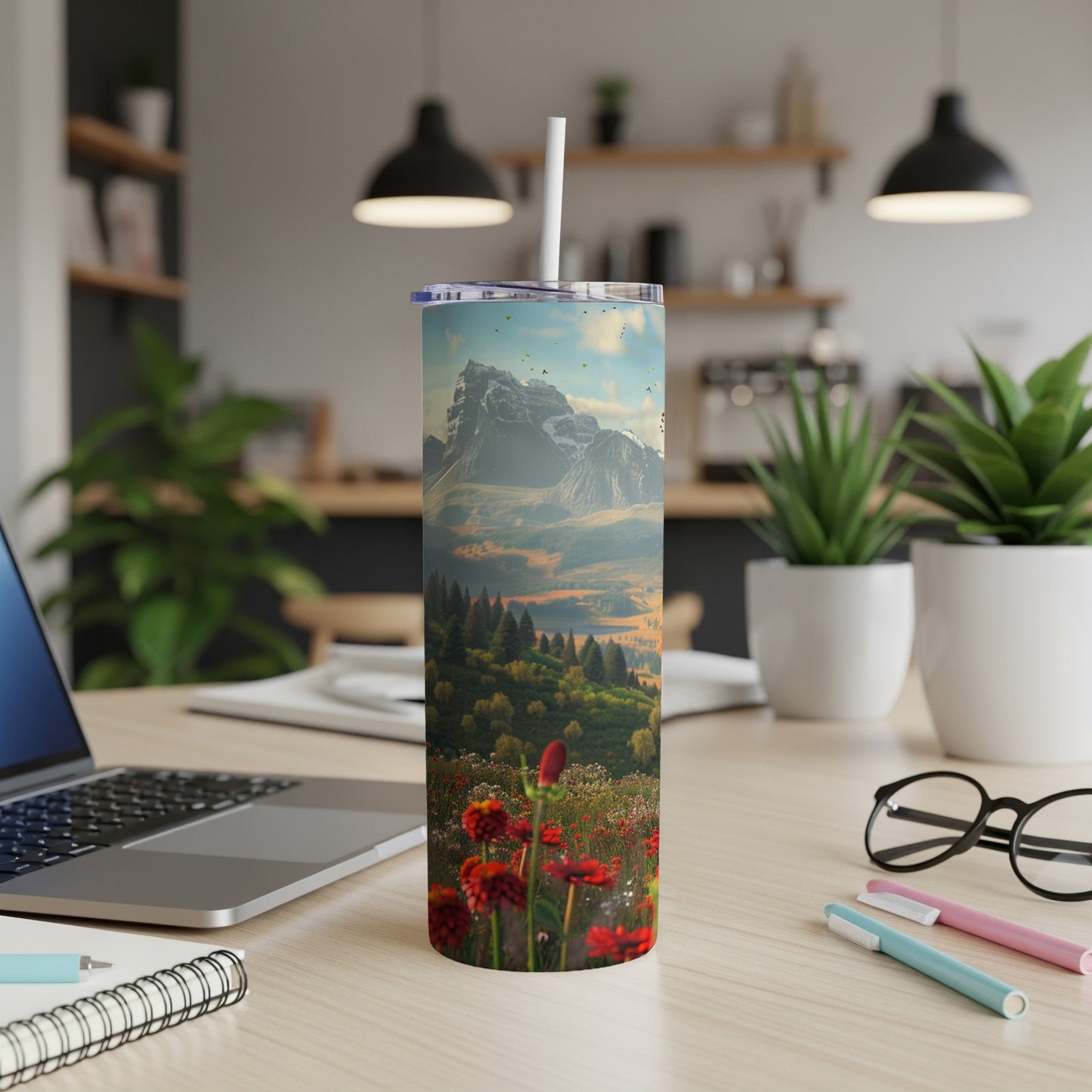 Tumbler with mountain landscape and red wildflowers on desk.