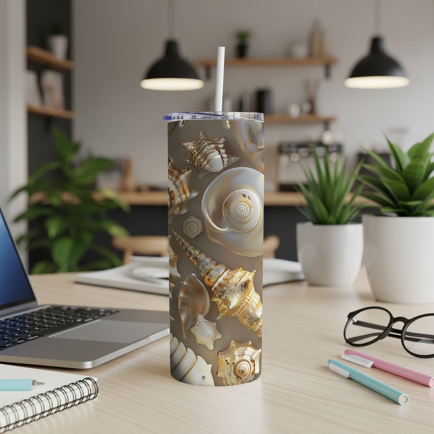 Seashell pattern on a stainless steel tumbler with straw on a desk.