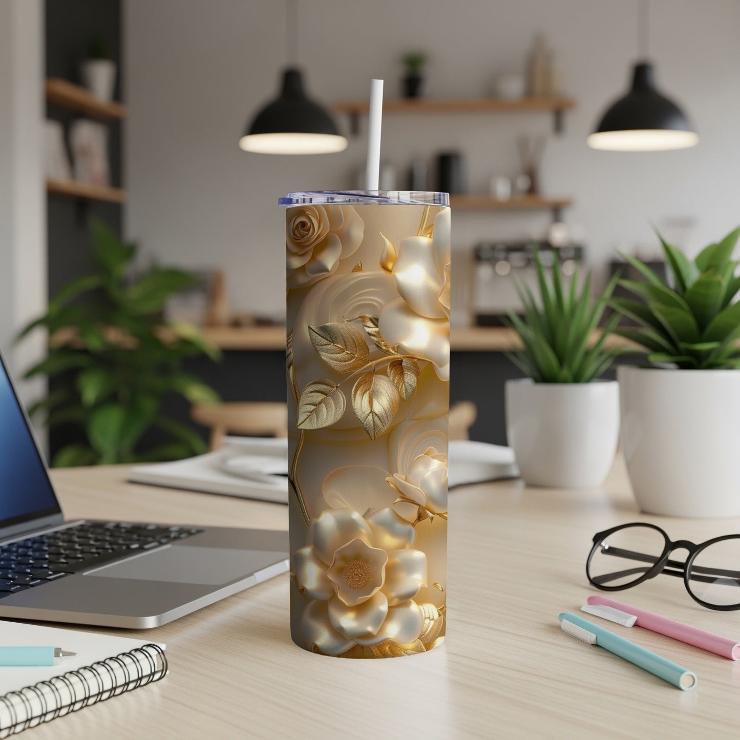 Gold floral tumbler with straw on a desk with laptop and pens.