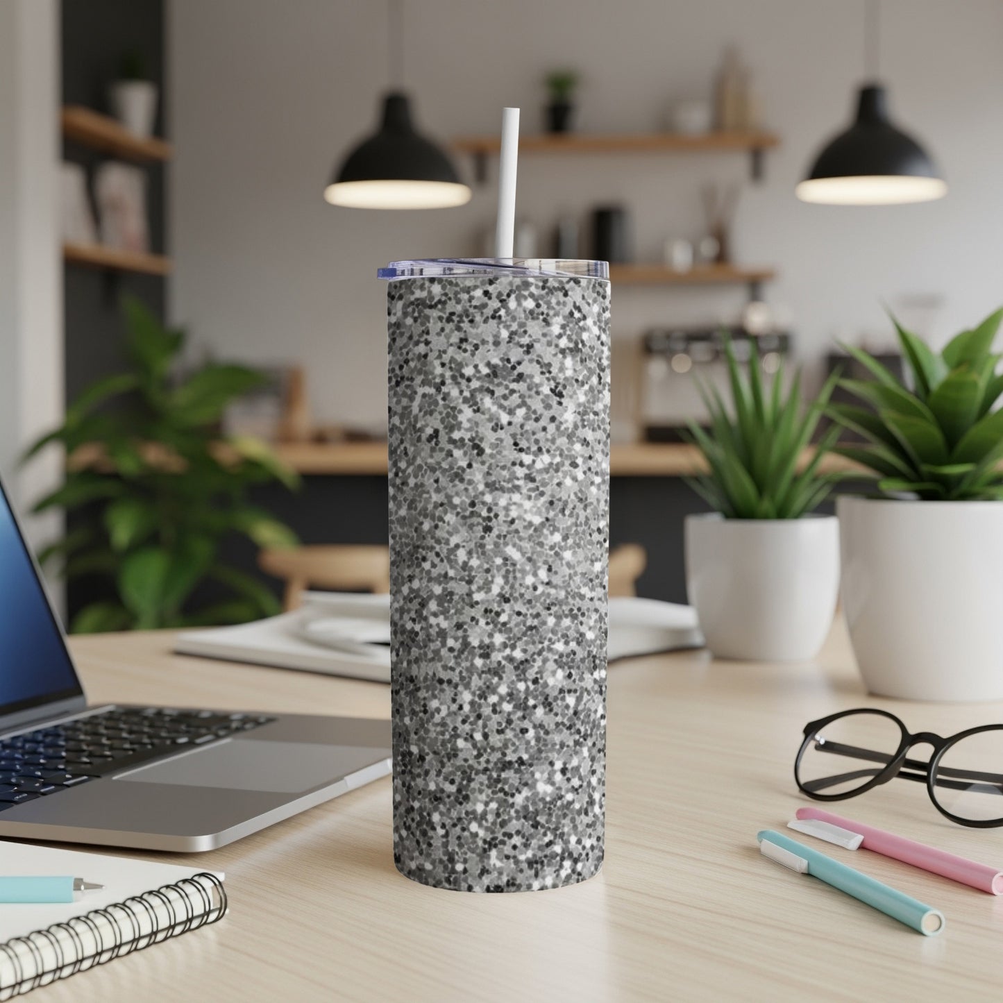Silver glitter tumbler with straw on a desk with a laptop.