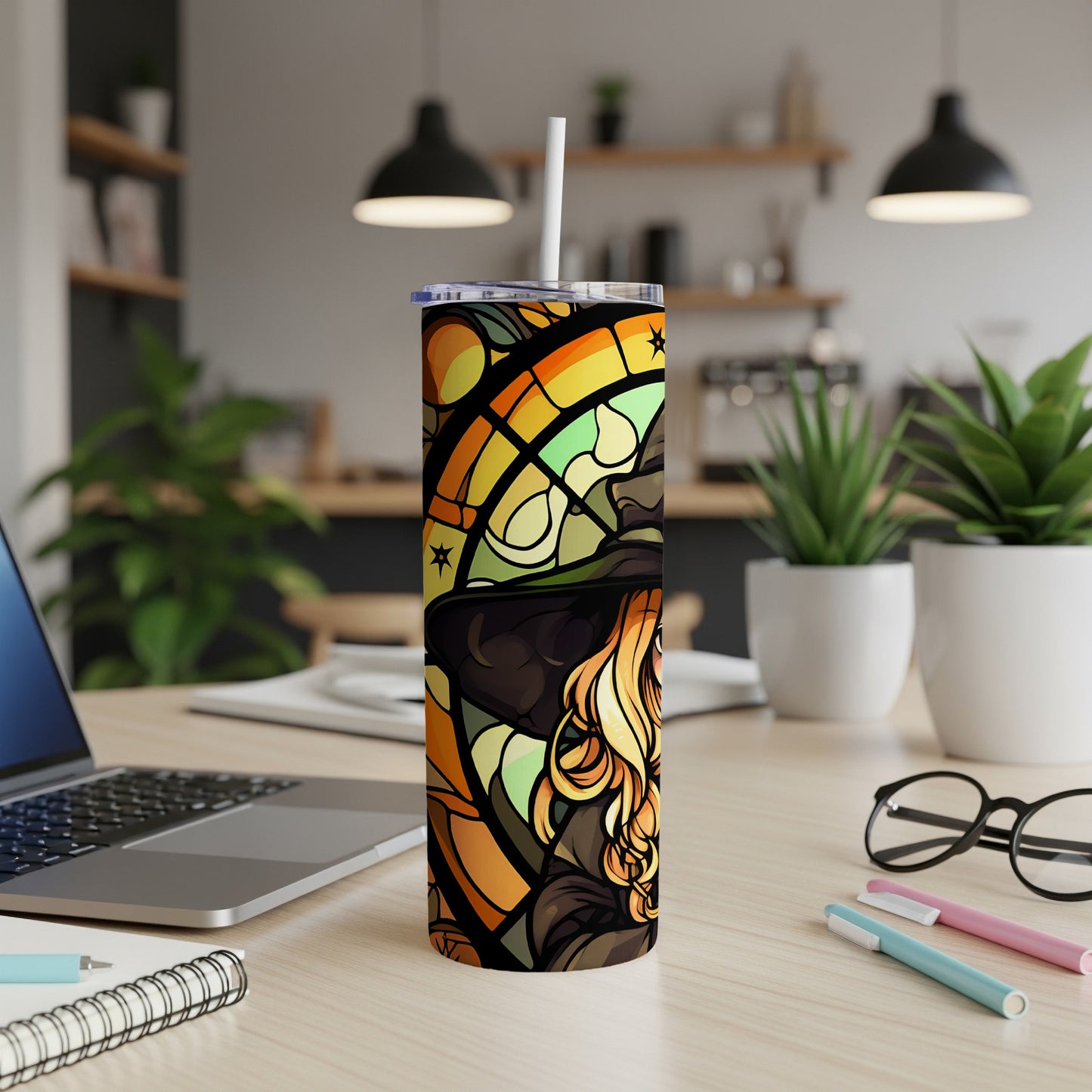 Tall tumbler with stained-glass witch design and straw, on a desk.
