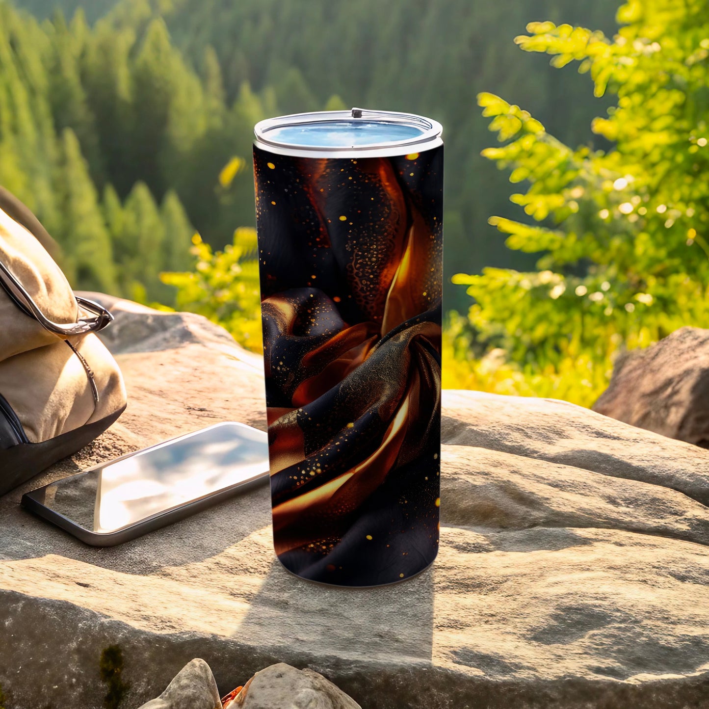 Tumbler with swirling black and gold fabric design on stone with backpack and phone.