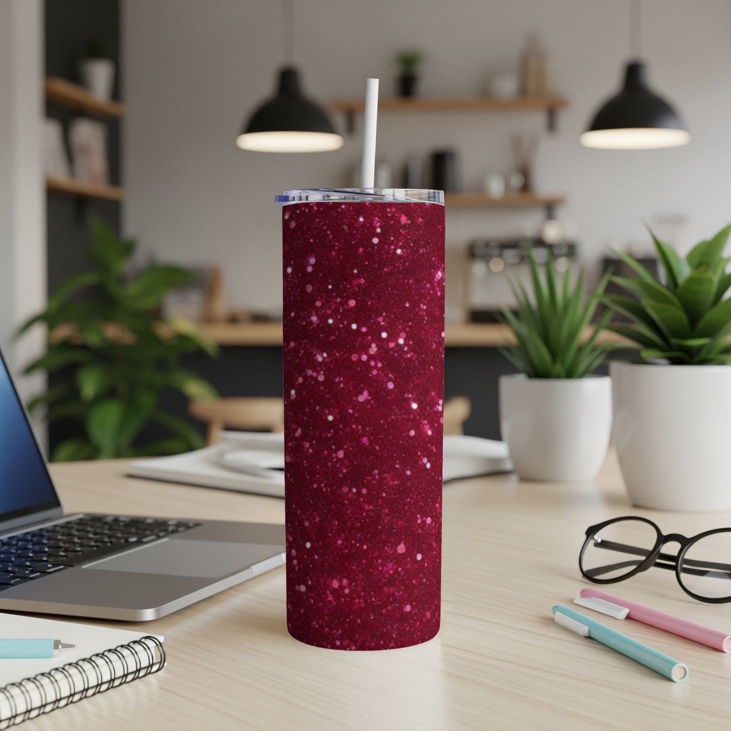 Glittering dark red skinny tumbler with a white straw on a desk.