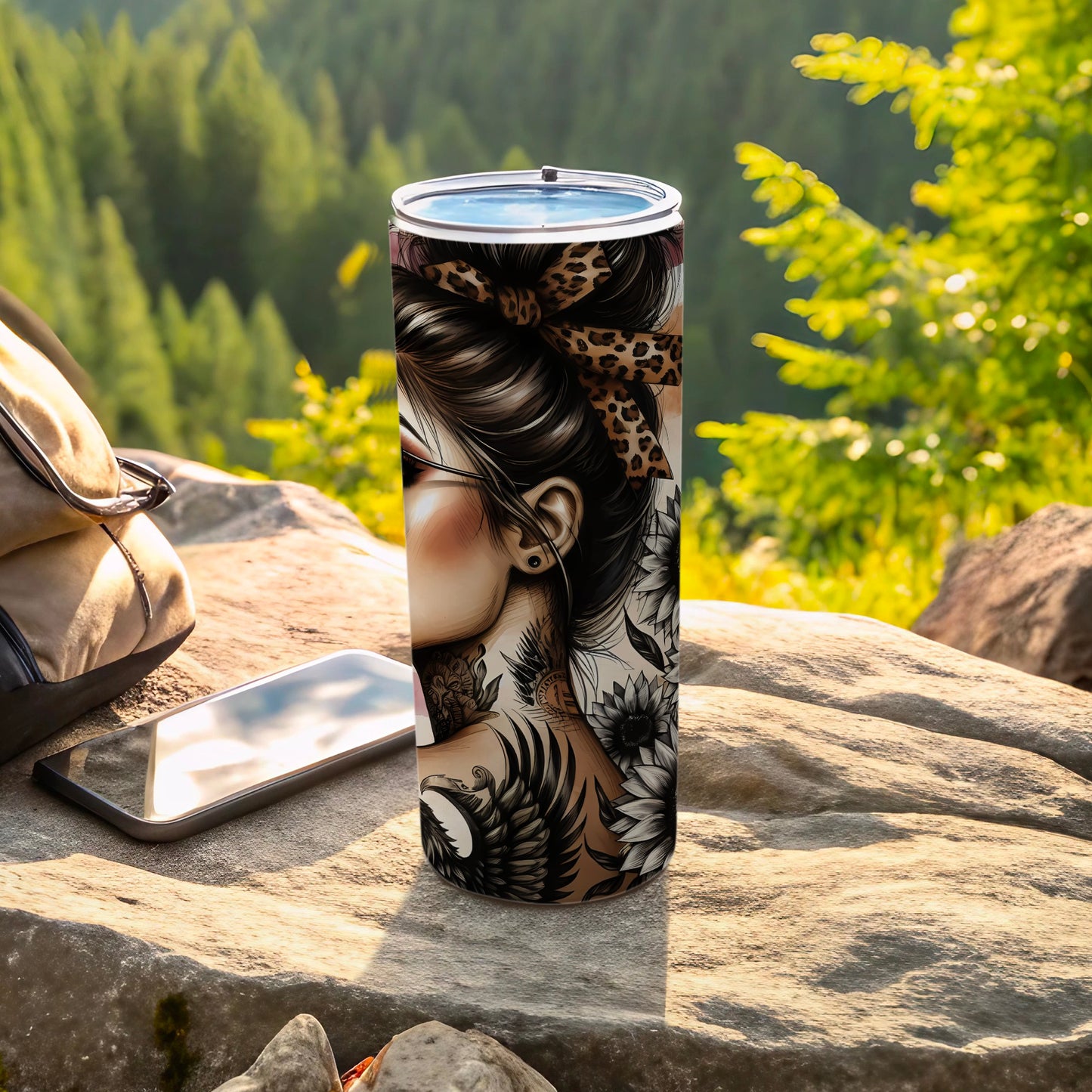 Tumbler with floral and tattoo design, beside phone and backpack outdoors.