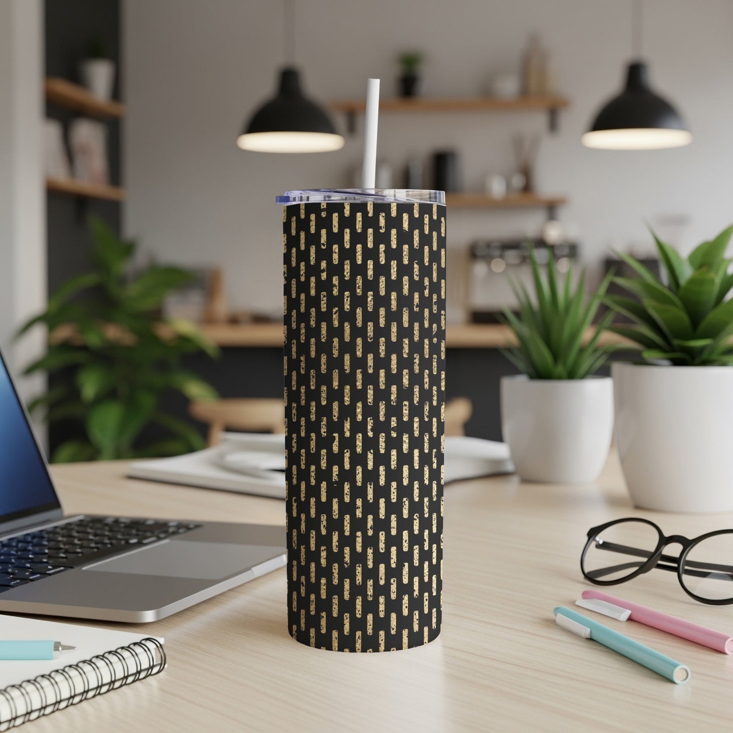 Black tumbler with gold dash pattern and straw on a desk.