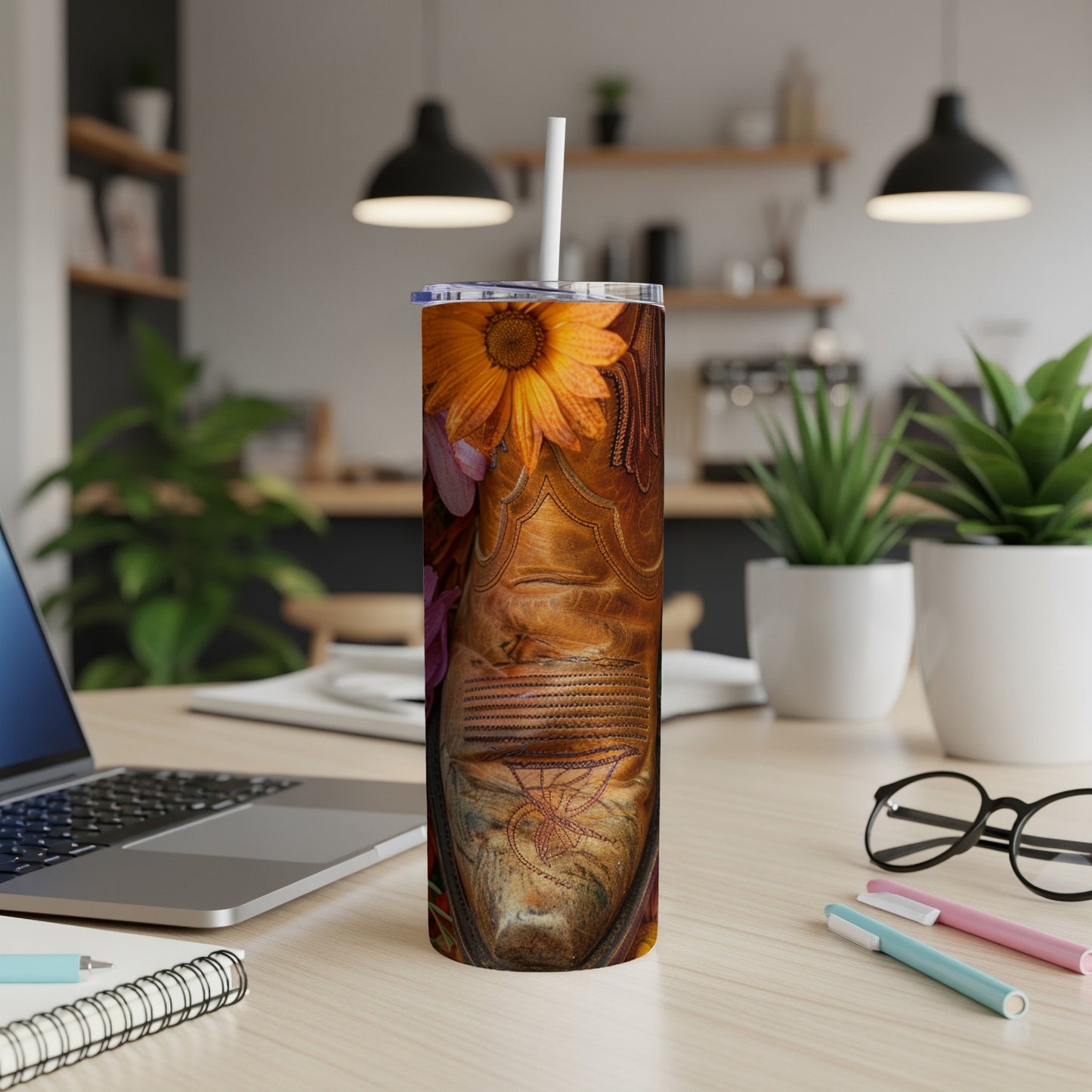 Cowboy boot with floral accents and a straw on a desk.