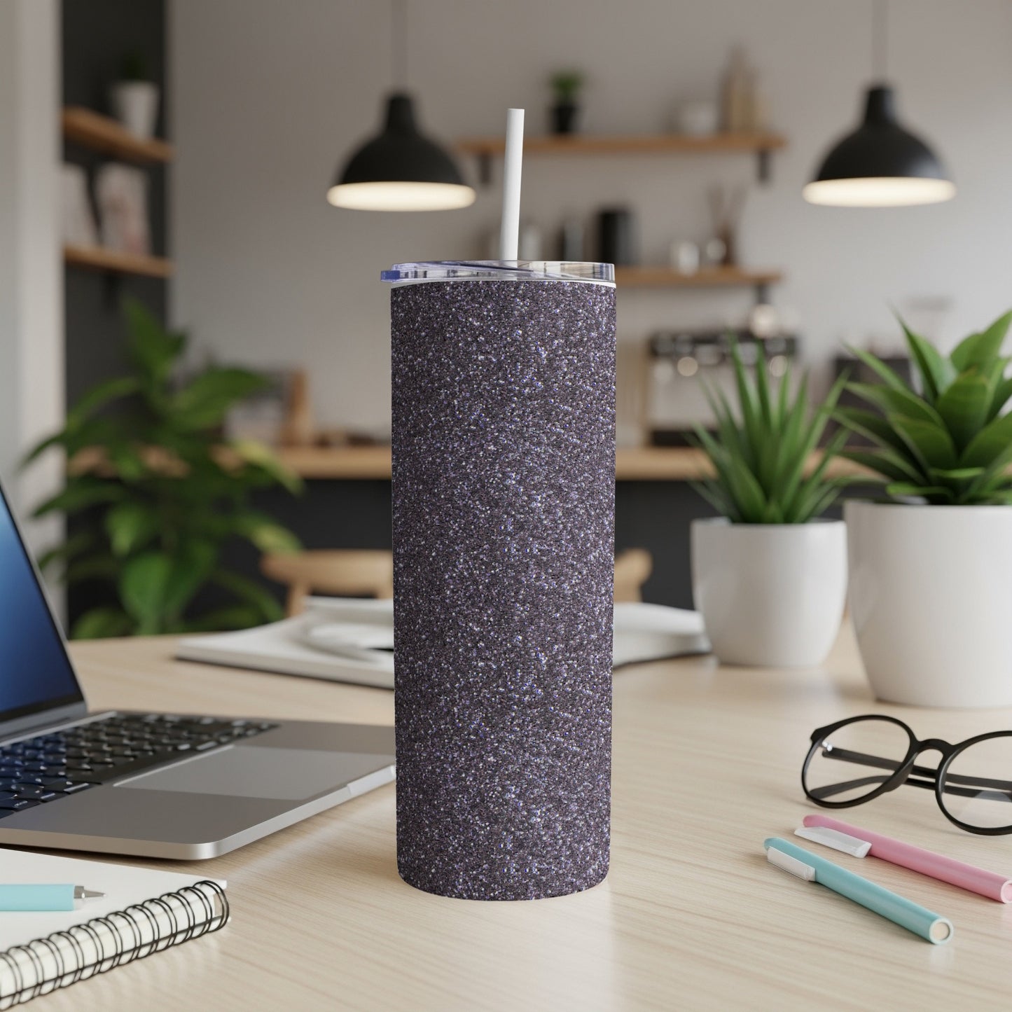 Glitter tumbler with straw on desk next to laptop and glasses.