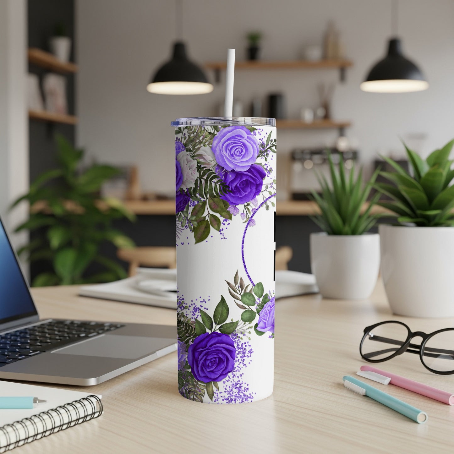 White tumbler with purple floral design and straw, on a desk.