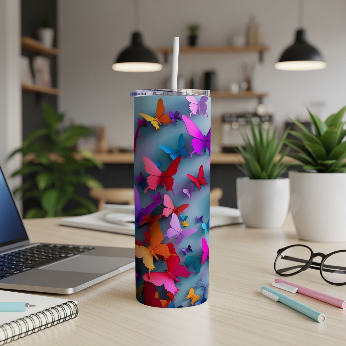 Colorful butterflies adorn a blue gradient tumbler with a straw on a desk.