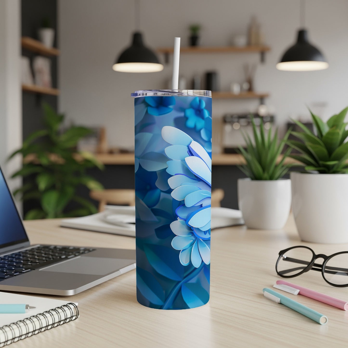 Blue floral tumbler with straw on desk with laptop and pens.