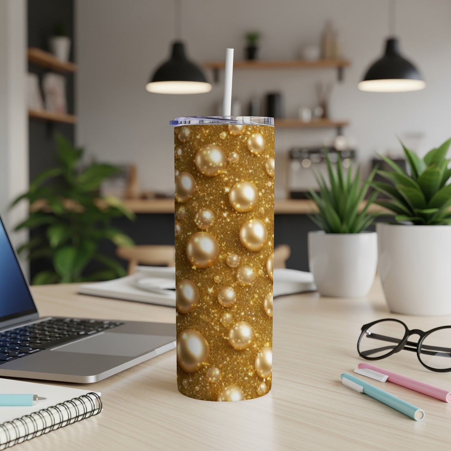 Glittering gold bubbles cover a stainless steel tumbler with straw on a desk.