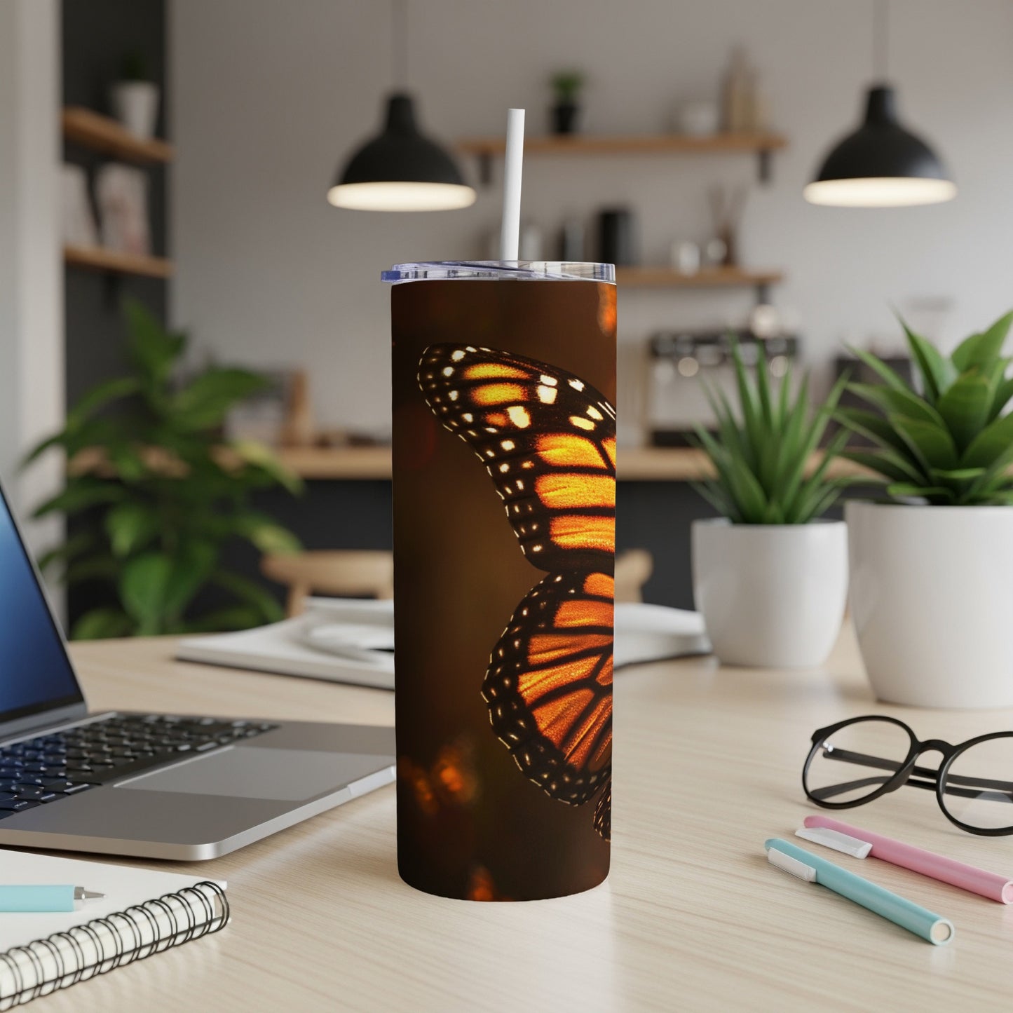 Monarch butterfly wings on a tall, skinny tumbler with a straw.