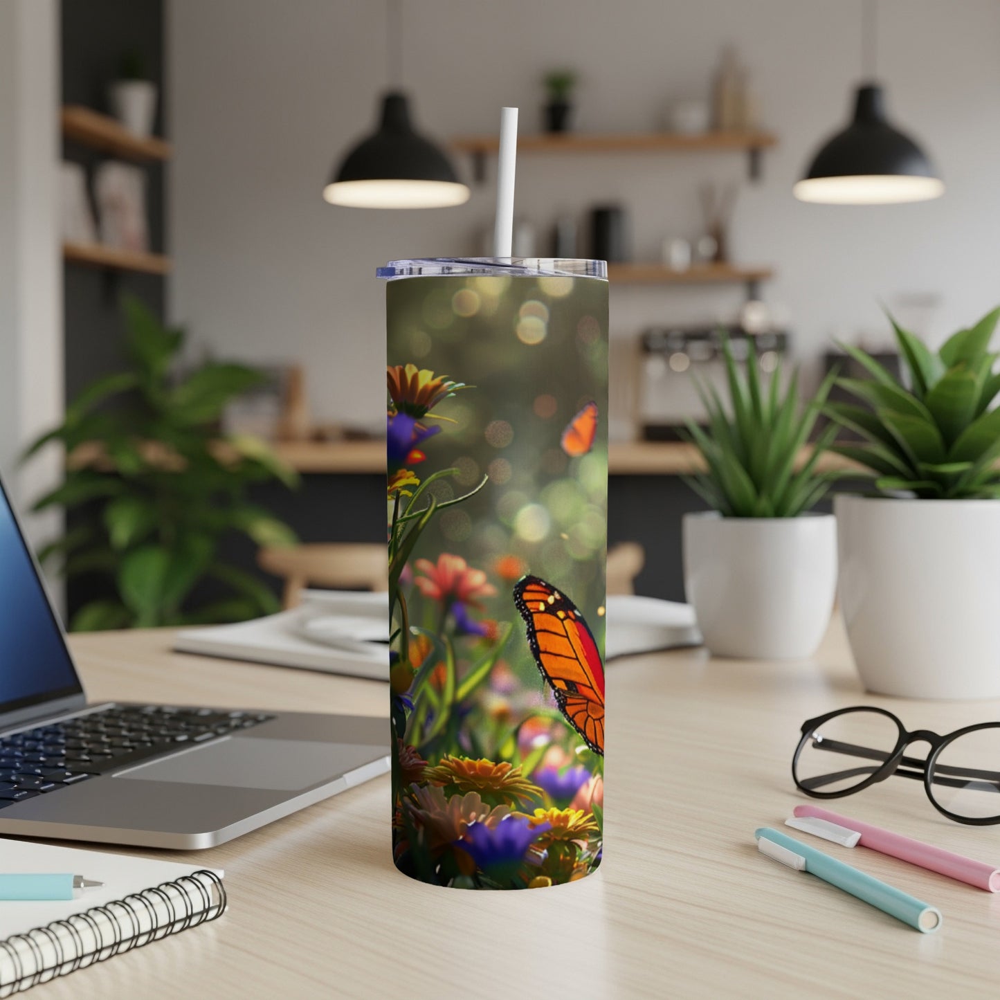 Orange butterfly on a floral tumbler with straw on a desk.