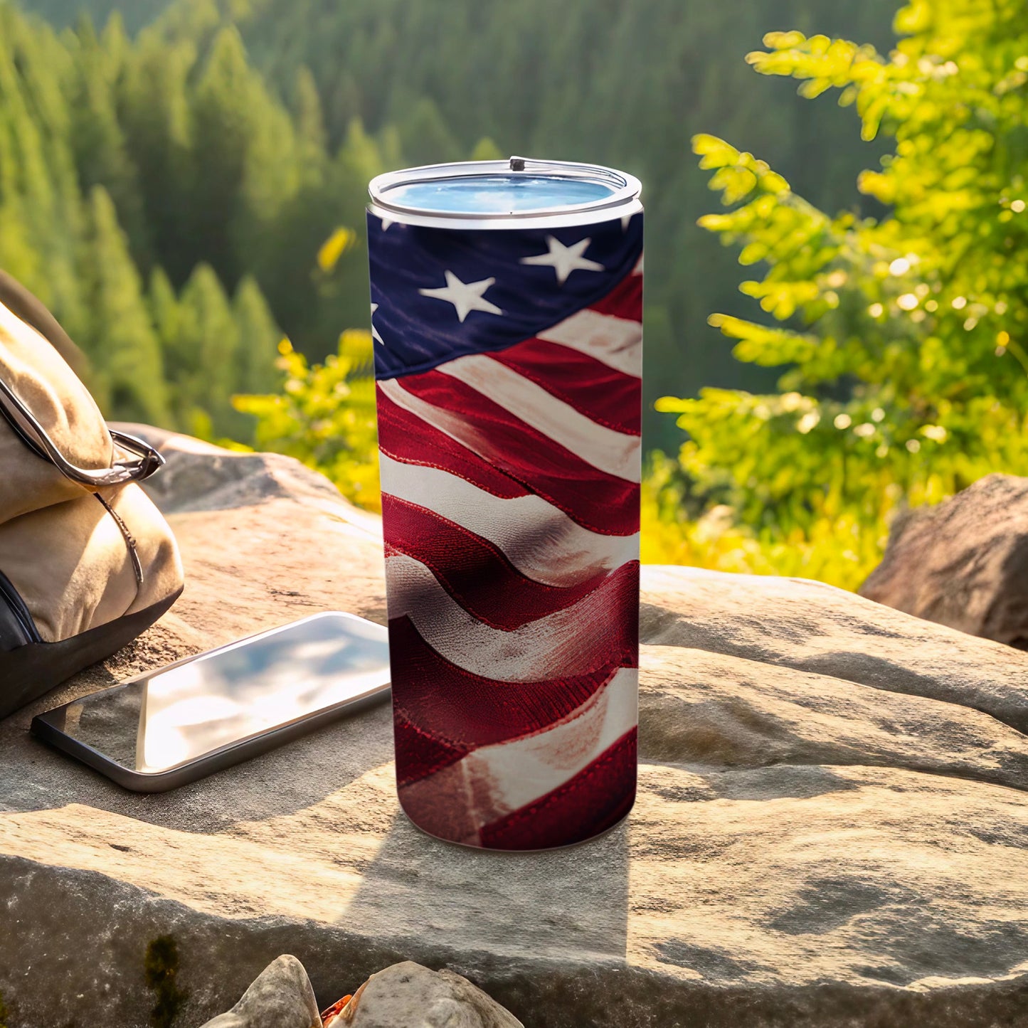 American flag tumbler with smartphone and backpack on rocks outdoors.