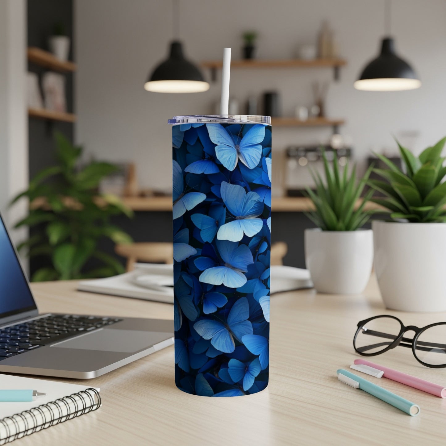 Blue butterflies cover a white tumbler with a straw on a wooden desk.
