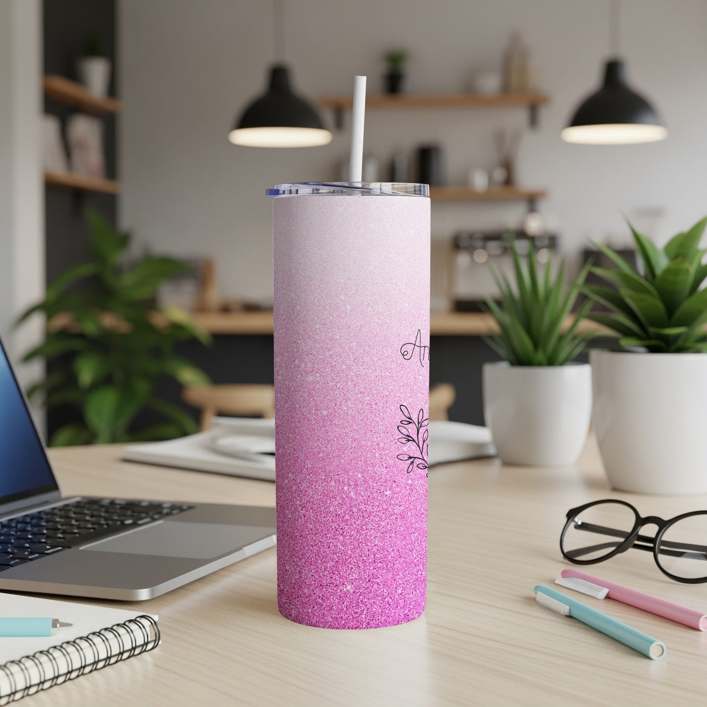 Pink glitter tumbler with floral design and straw on desk.