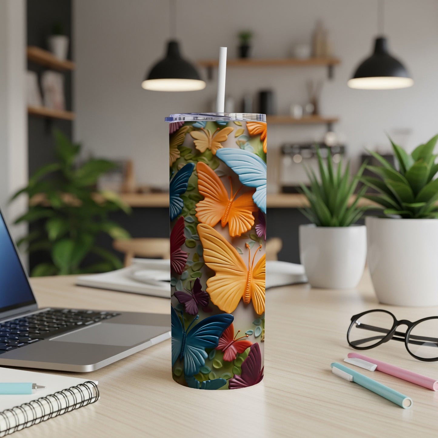 Tall tumbler with colorful embossed butterflies, a straw, and a laptop on a desk.