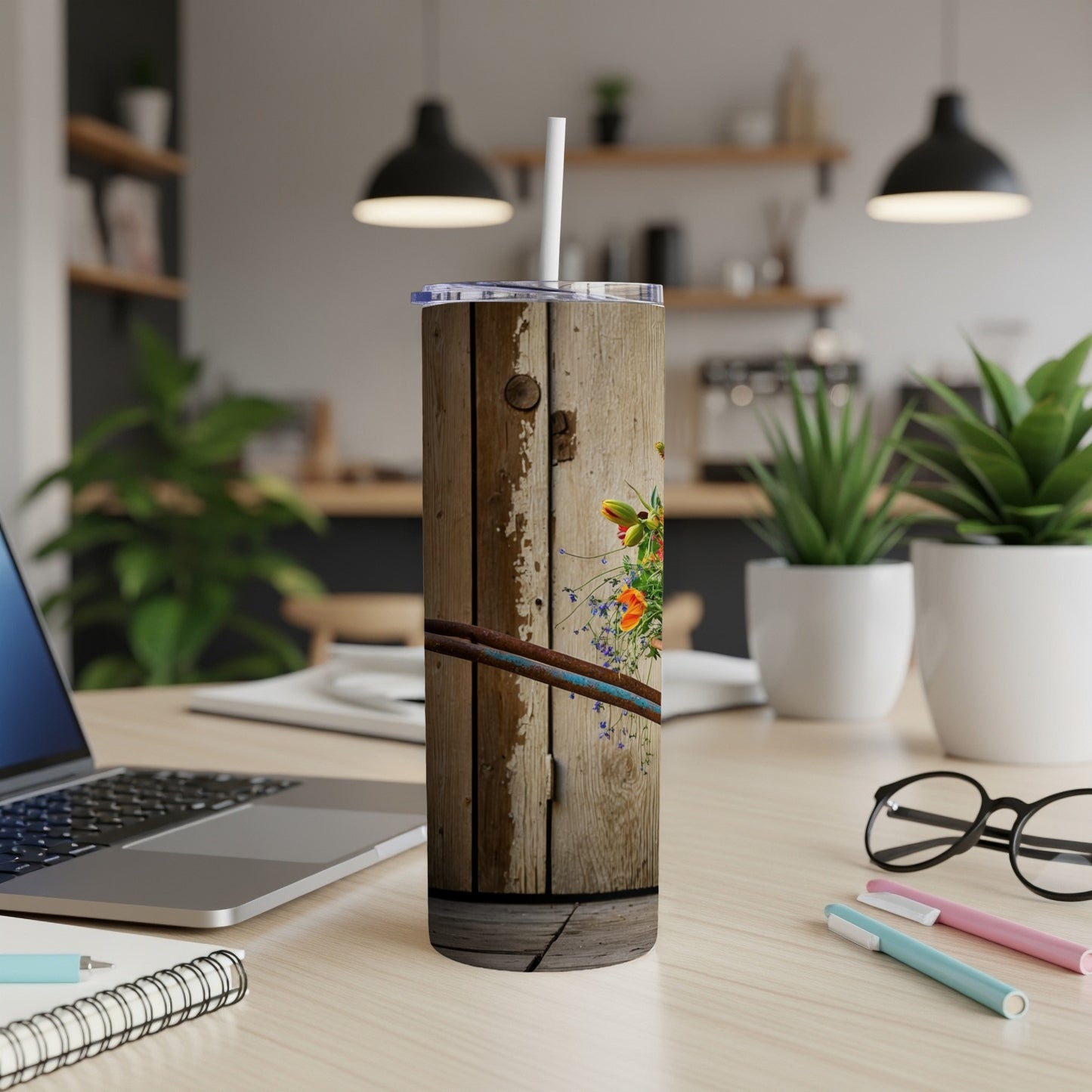Wooden tumbler with wildflowers and blue straws on a desk.