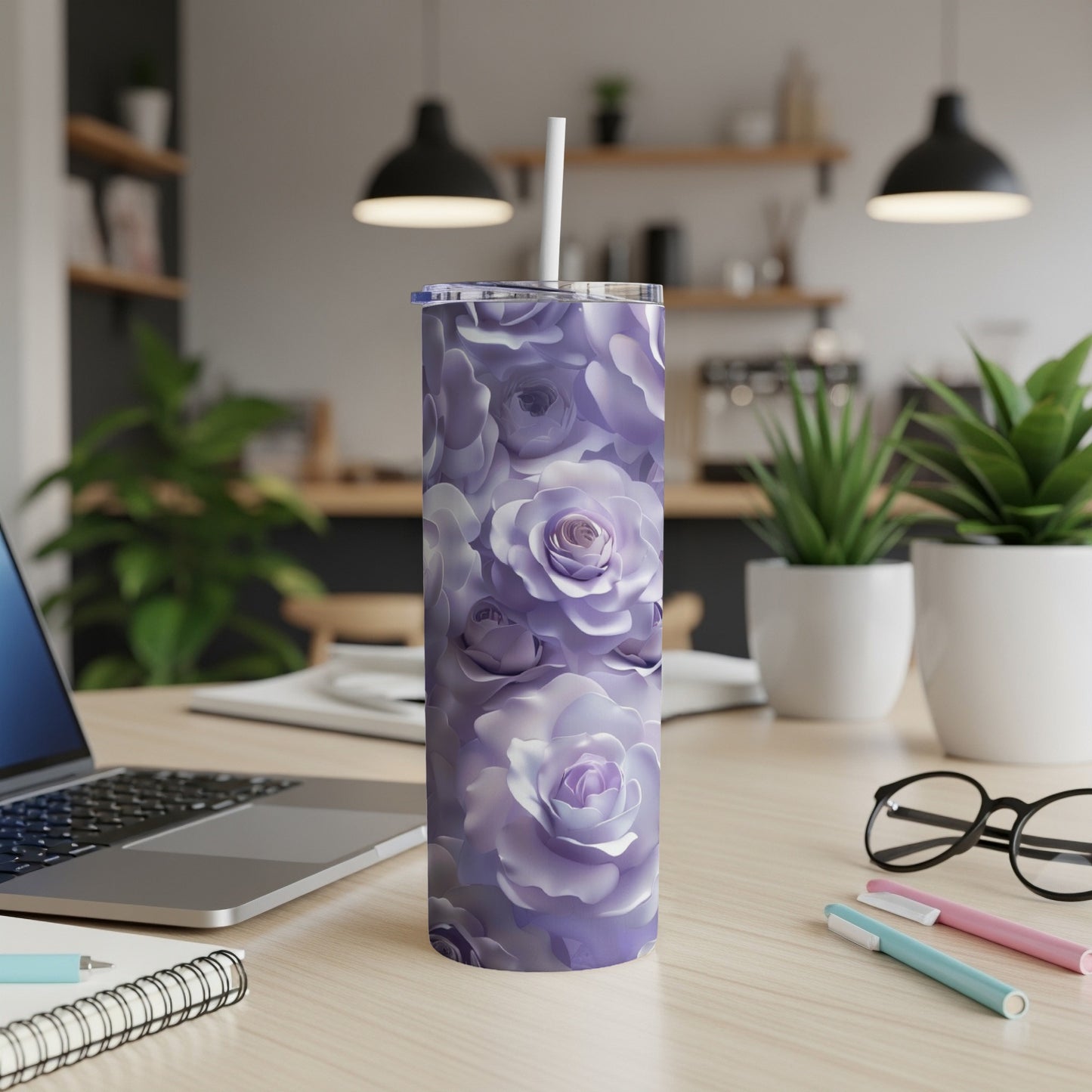 Purple floral tumbler with straw on desk next to laptop and pens.