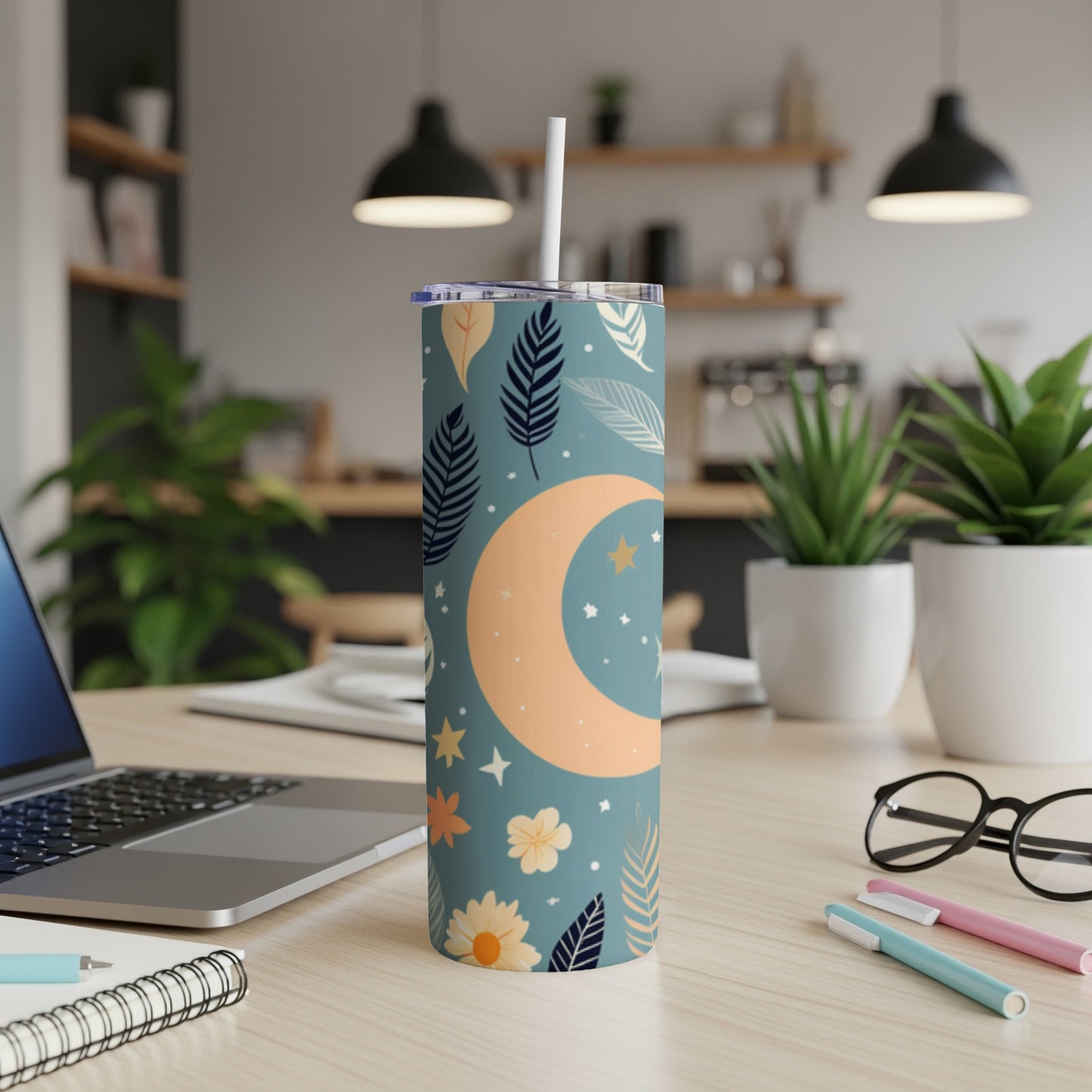Tall teal tumbler with moon and star pattern, on a desk.