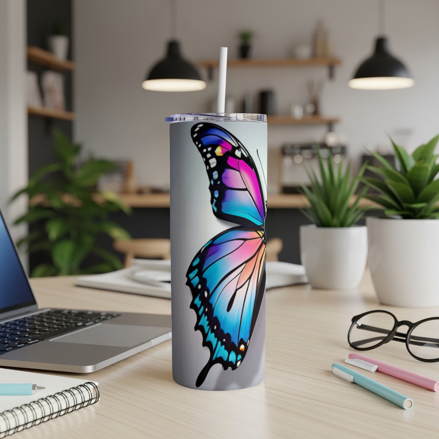 Tumbler with colorful butterfly design on a desk with laptop.