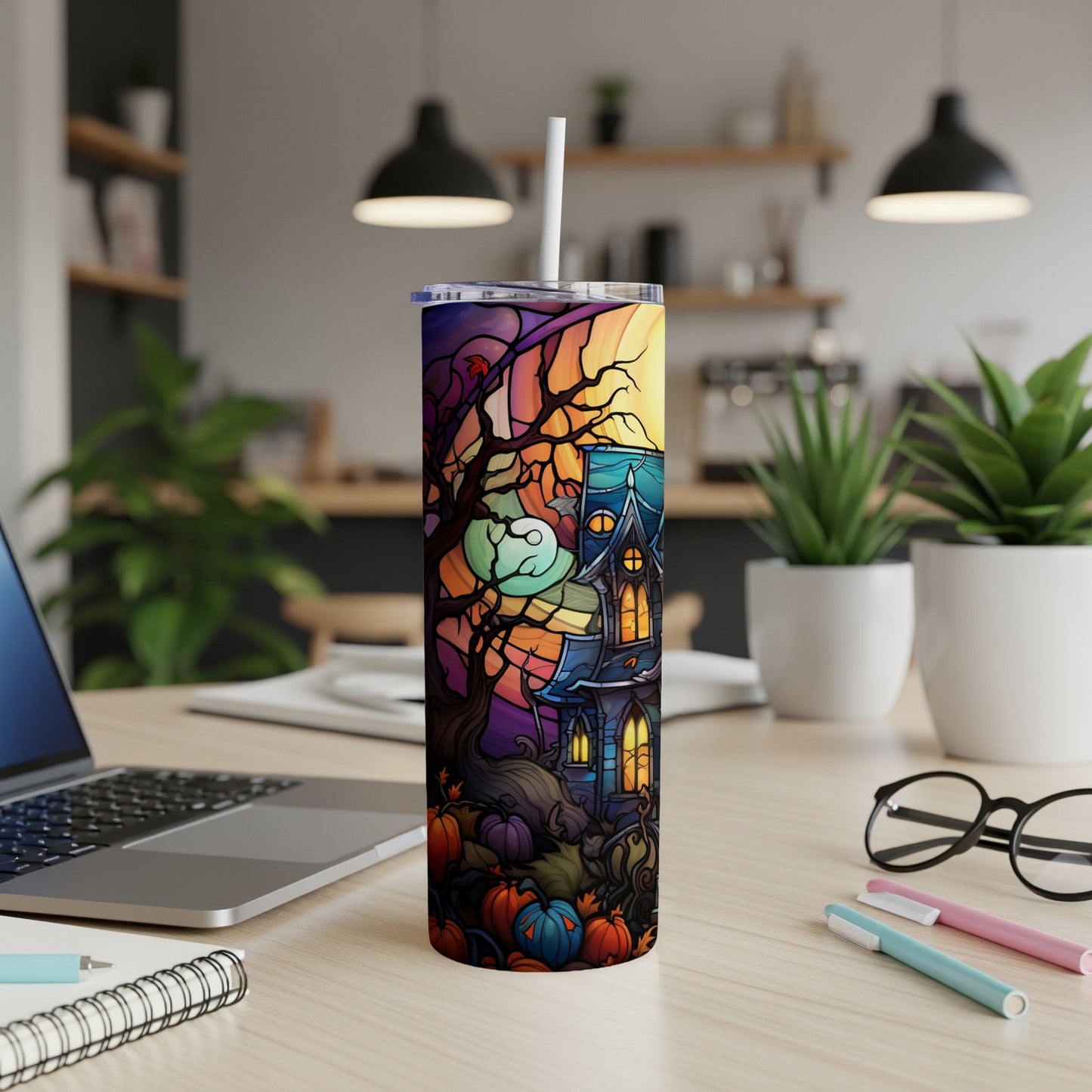 Halloween tumbler with haunted house and pumpkins, on desk.