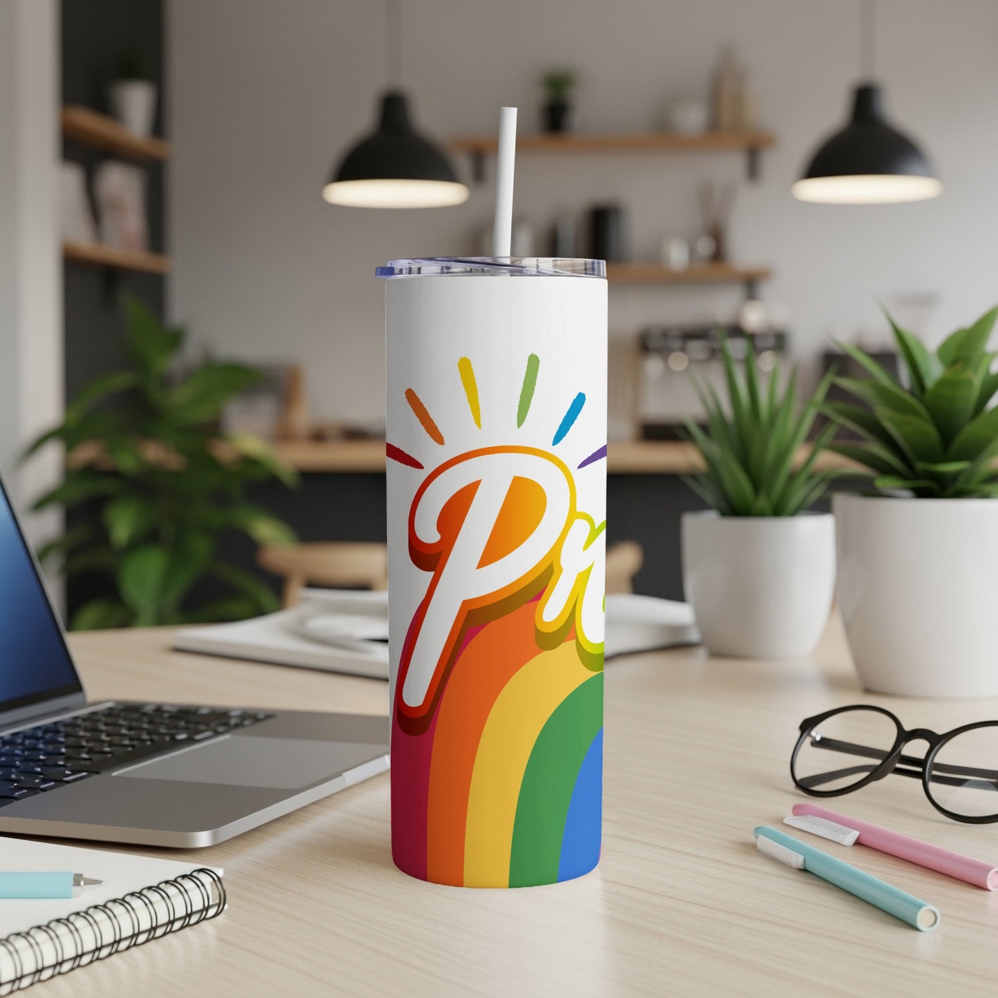 Pride tumbler with rainbow graphic on a desk with a laptop.